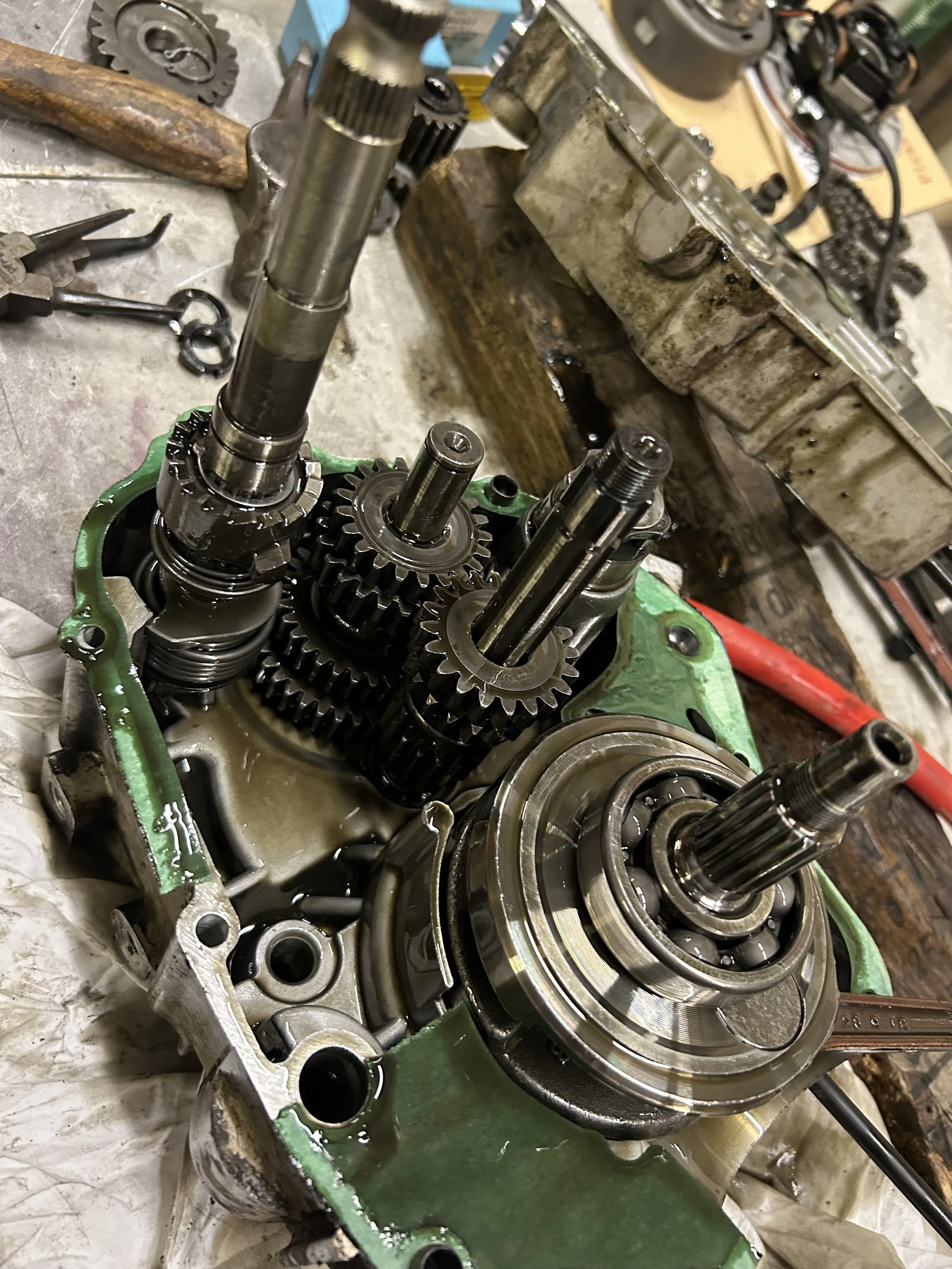 Disassembled motorcycle engine with gears, shafts, and bearings on a workbench.