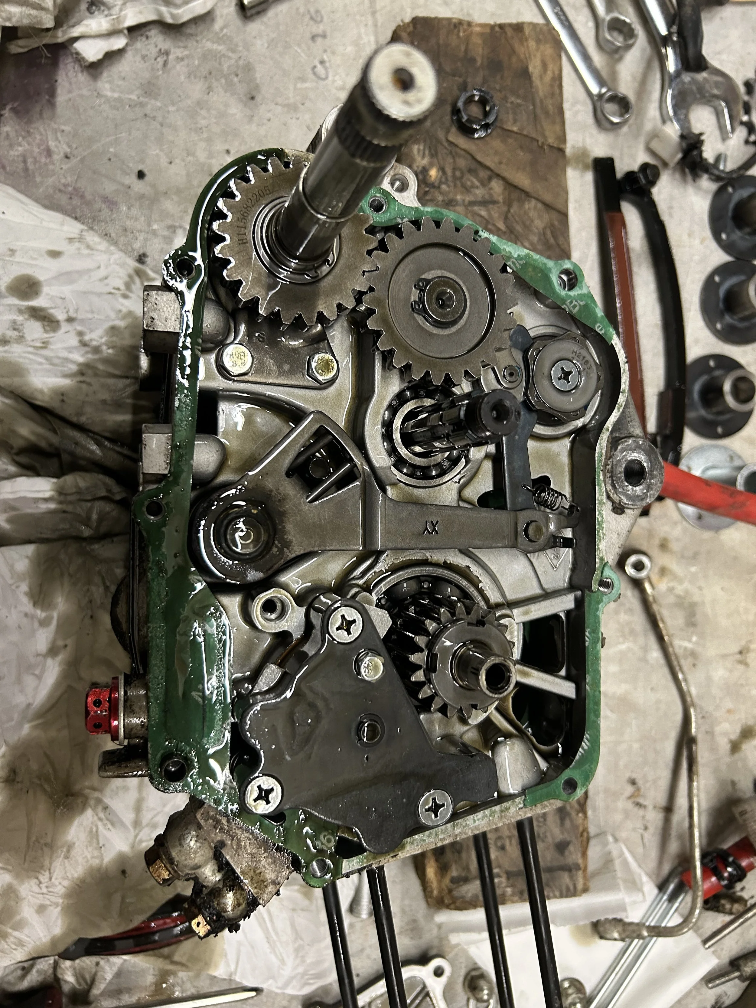 Mechanical engine components being assembled or repaired, with gears, shafts, and bolts on a workbench surrounded by tools.