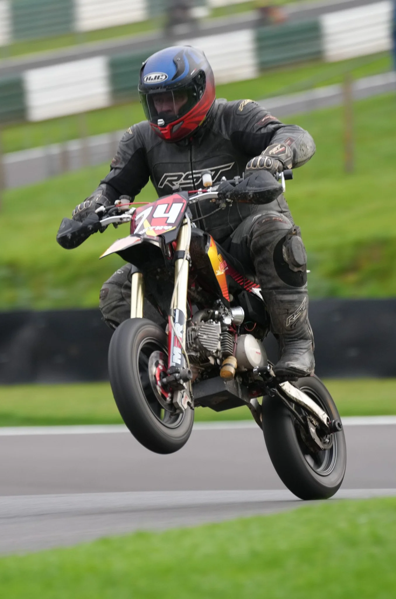 Motorcyclist performing a wheelie on a racing bike on a track, wearing a black racing suit and a black helmet.