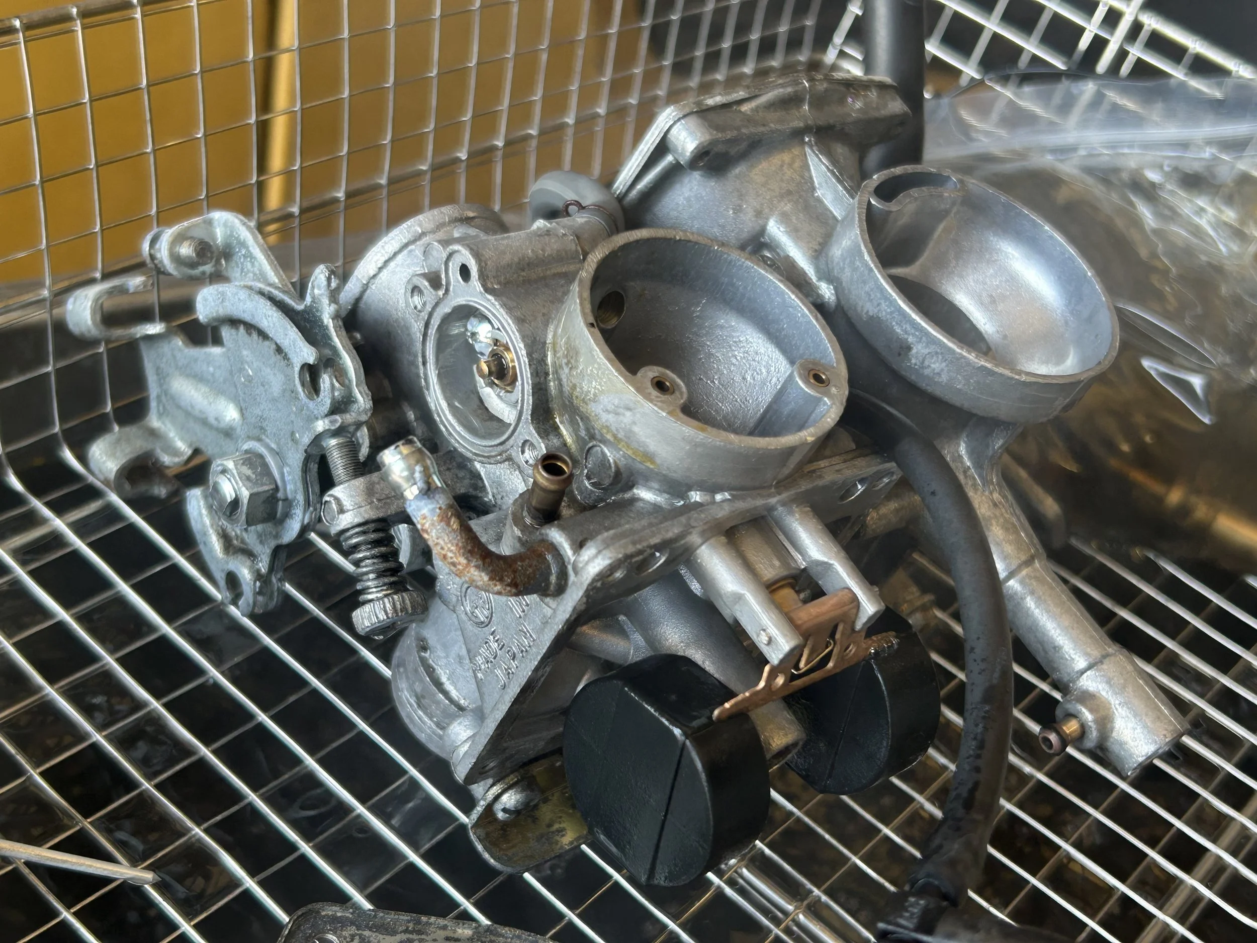 A disassembled carburetor with two large round openings, on a metal wire shelf.