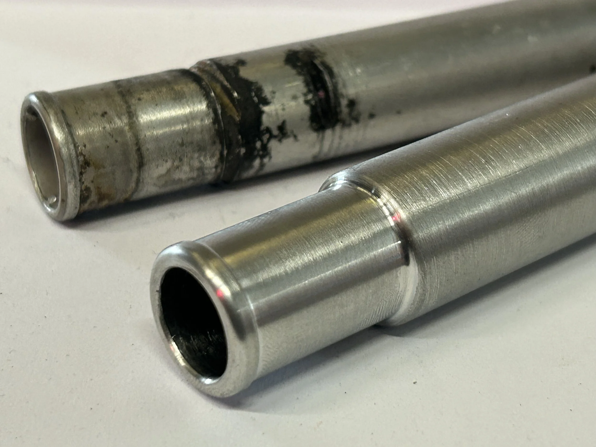 Close-up of two metal hydraulic or pneumatic cylinders, one old and worn, the other new and polished.