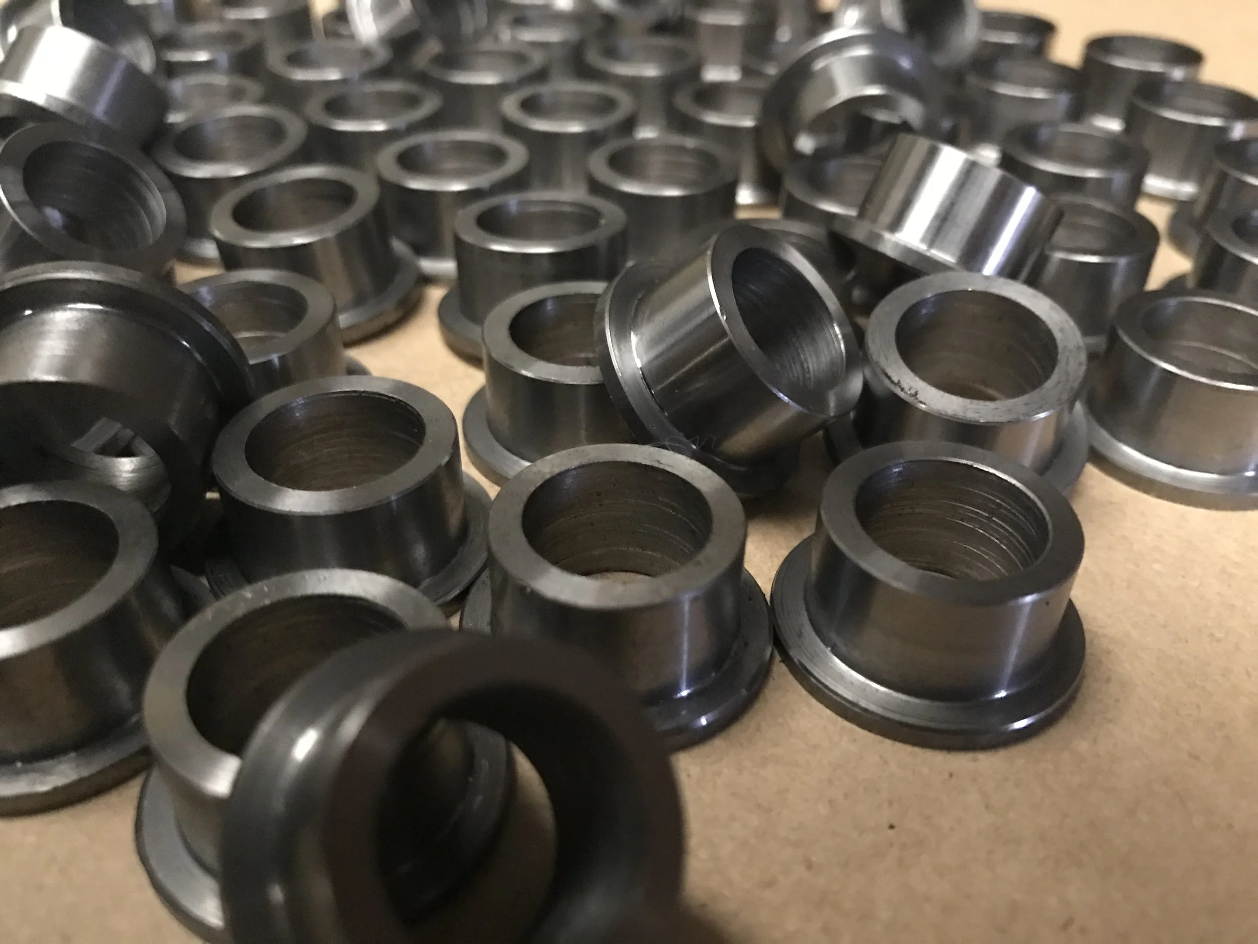 Multiple small, metallic, industrial washers or spacers scattered on a flat surface.