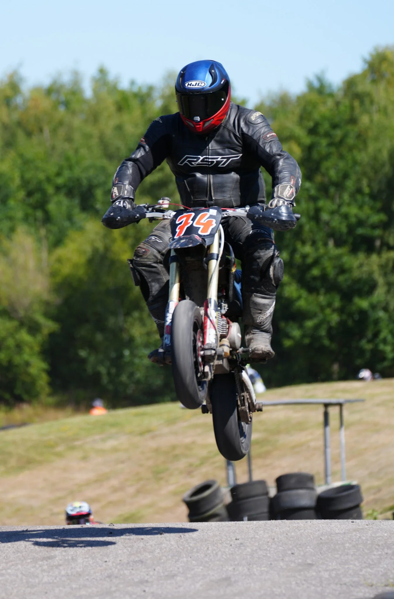 Motocross rider in black gear and helmet jumping over a ramp on a dirt track.