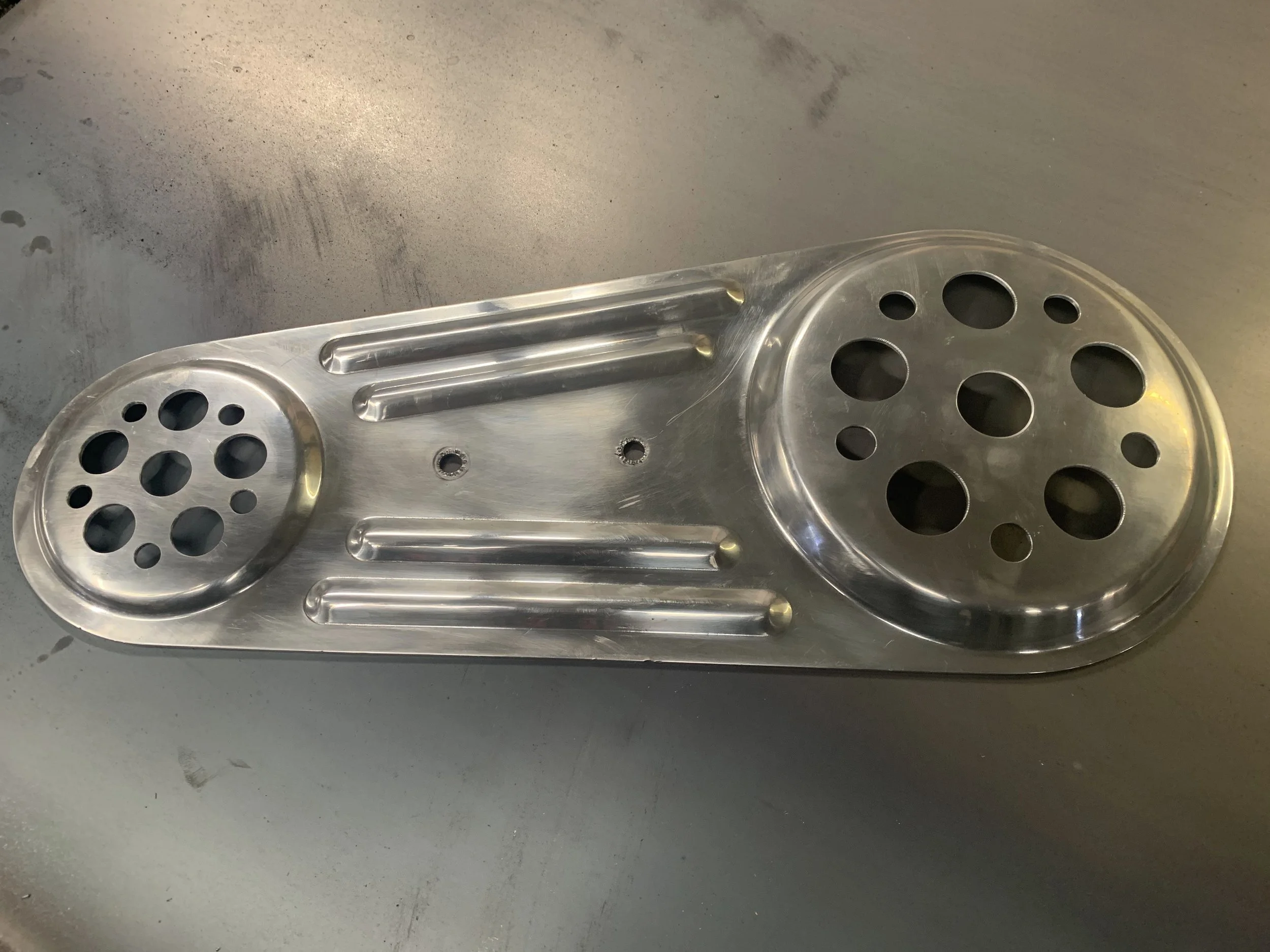 A metallic object with two circular sections, each containing multiple holes, connected by three parallel bars.