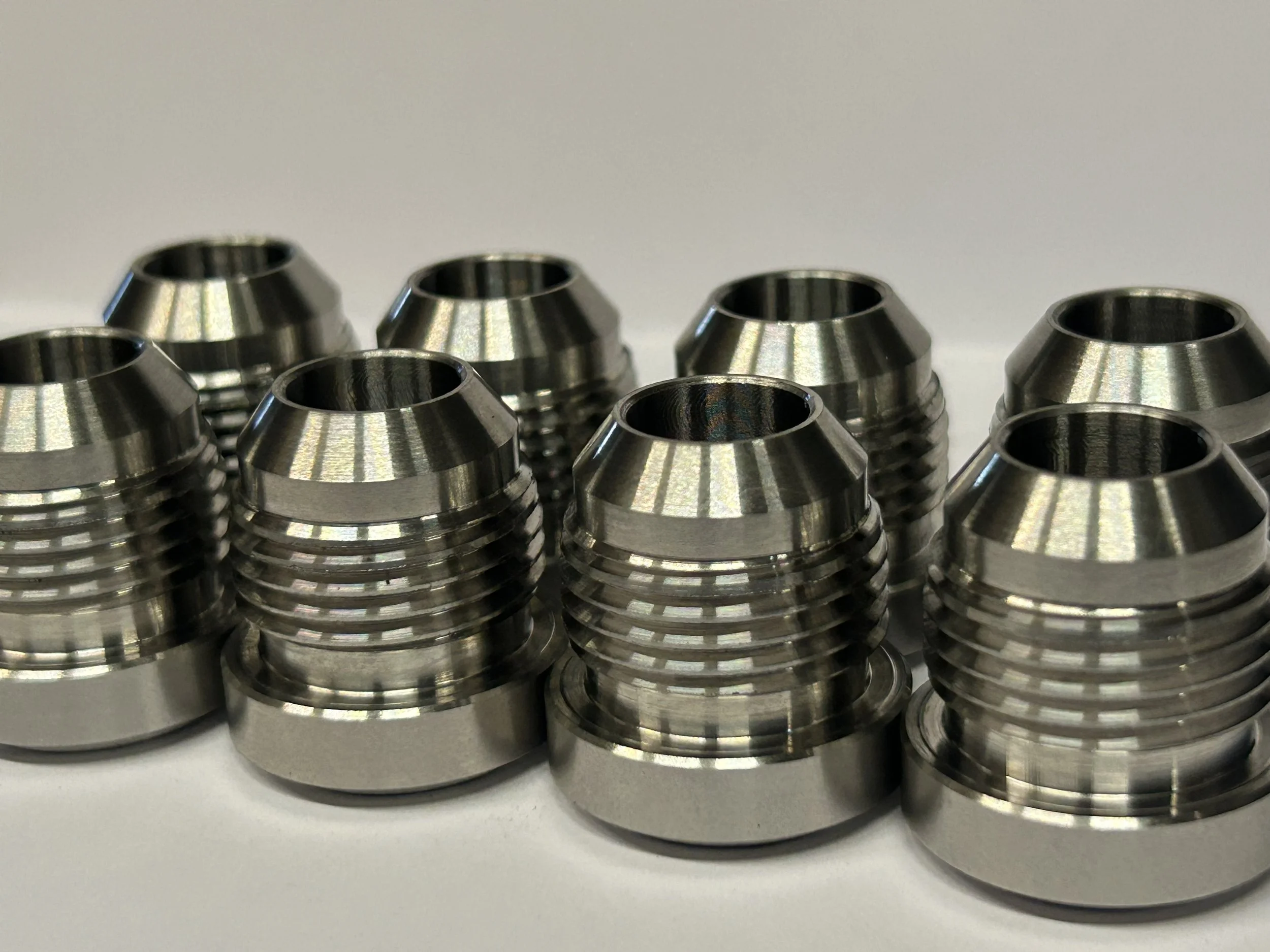Multiple metal threaded nuts arranged in rows on a white surface