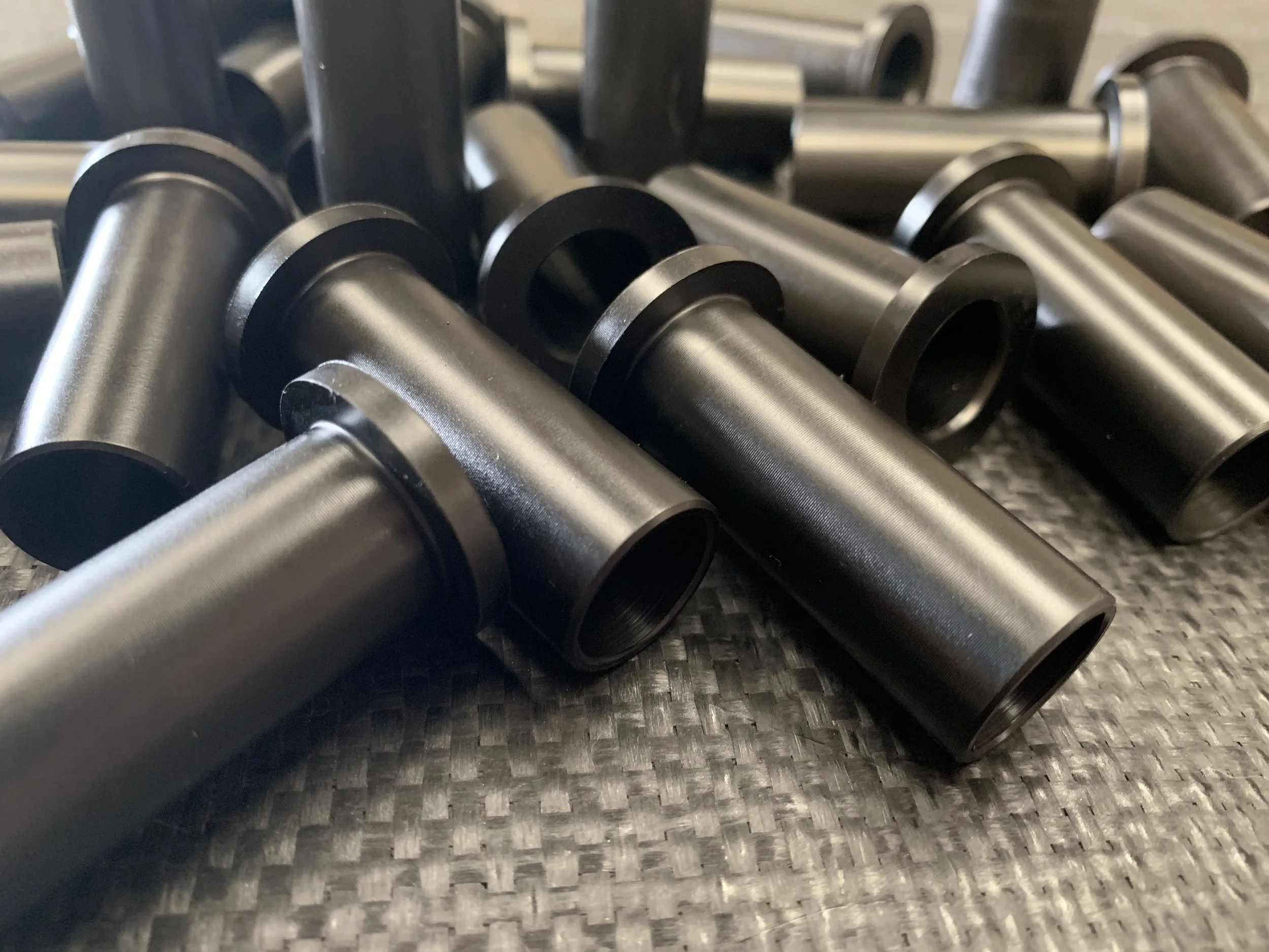 A close-up of several black cylindrical metal components with flanges on a textured surface, possibly parts of a machine or equipment.