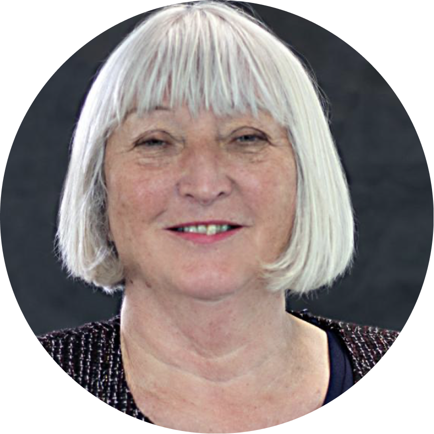 Close-up of our co-inventor, Sheila MacNeil, a smiling woman with short, gray hair and light skin, wearing a dark top with sequined shoulders, against a dark background.