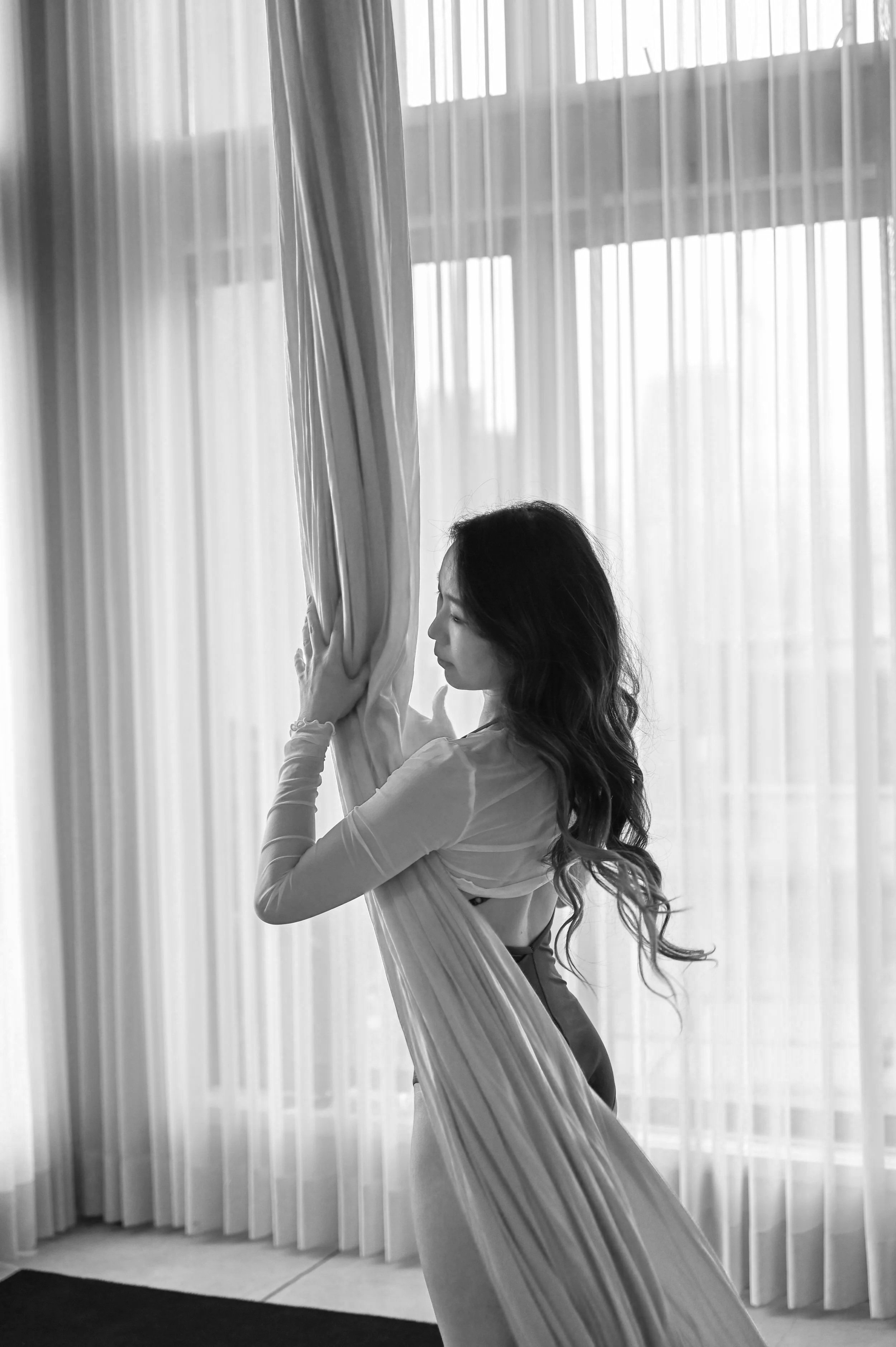 A woman with aerial silks in front of large windows with sheer curtains.