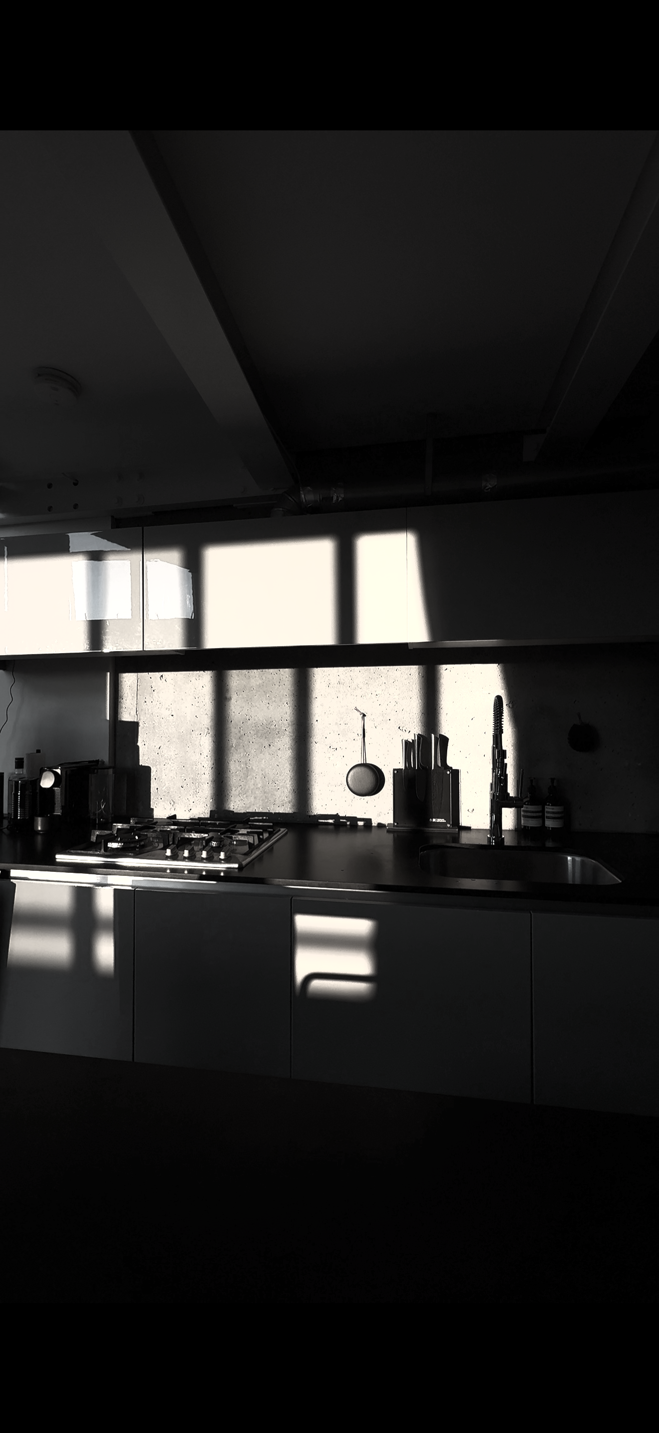 Sunlight streaming through window, casting shadows on kitchen counter with stove, sink, and kitchen utensils.