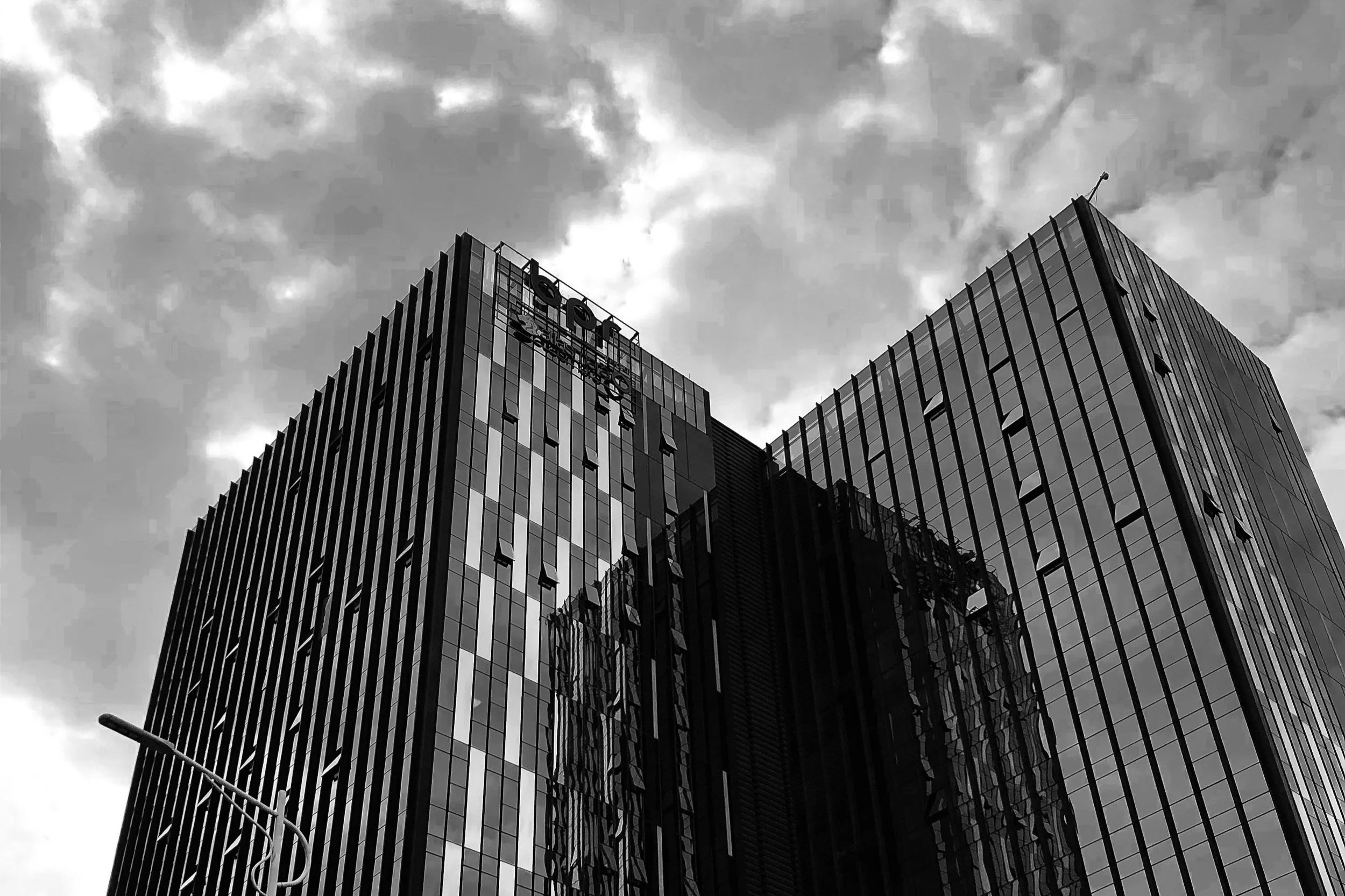 A black-and-white photo of modern glass high-rise buildings with reflections, under a cloudy sky.