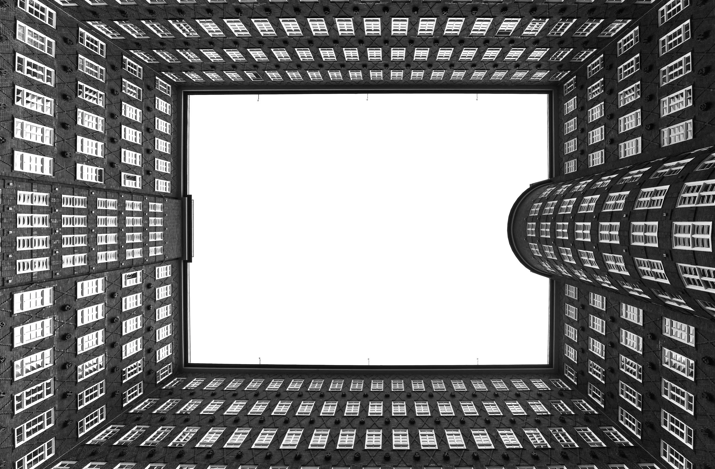 Black-and-white photo of a courtyard surrounded by tall brick buildings with many windows, viewed from the bottom looking up at the open sky.