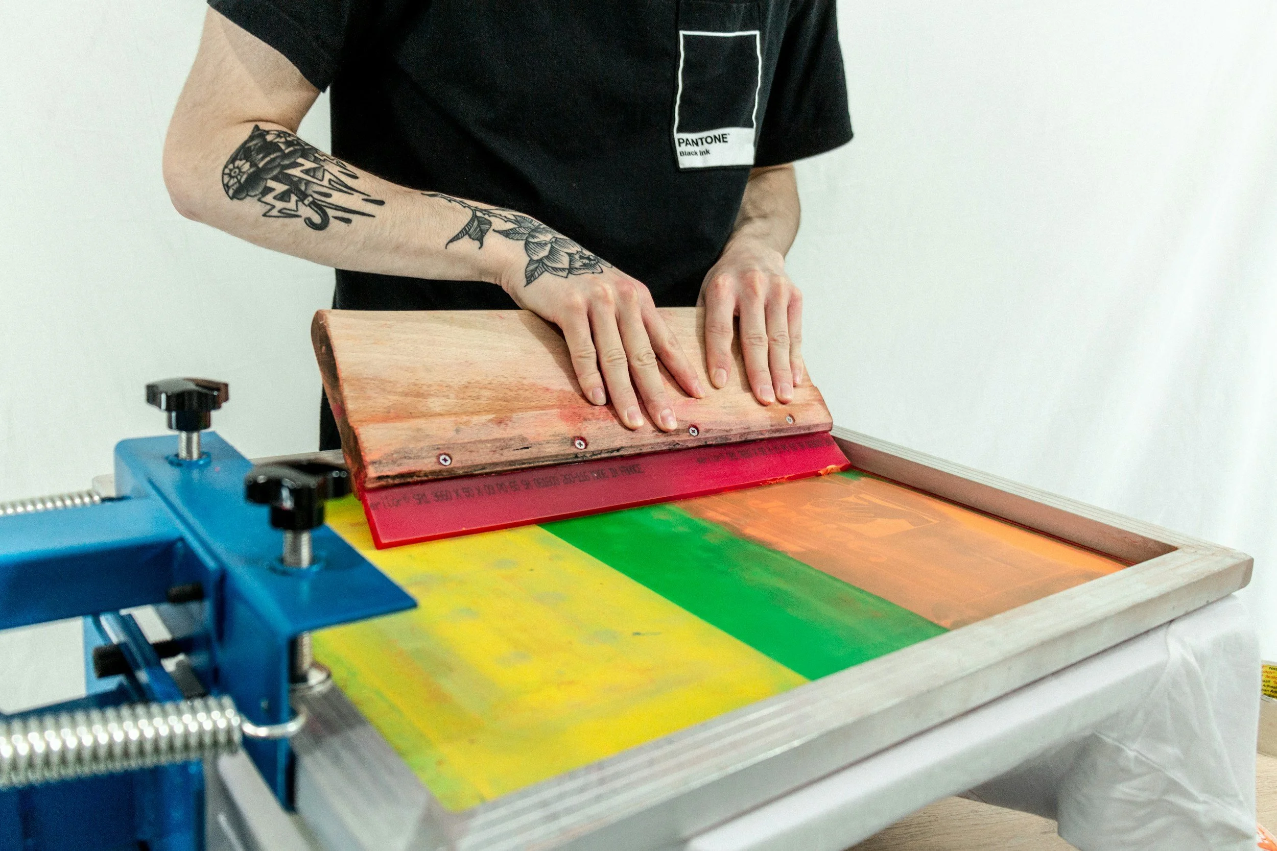 Beim Siebdruck entstehen durch Handarbeit besonders intensive Farben und individuelle Ergebnisse. Ein Person druckt mehrfarbig auf ein Textil mit einer SIebdruckmaschine.