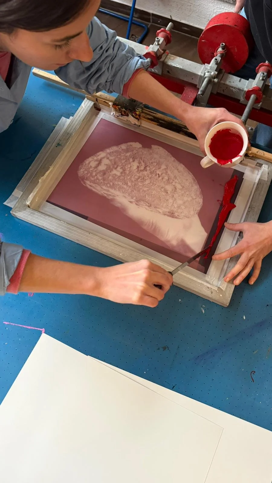 Personen bei der Siebdruck Arbeit, die roten Farbdinger und Hand Sabers verwenden, um ein Bild auf Papier zu drucken.