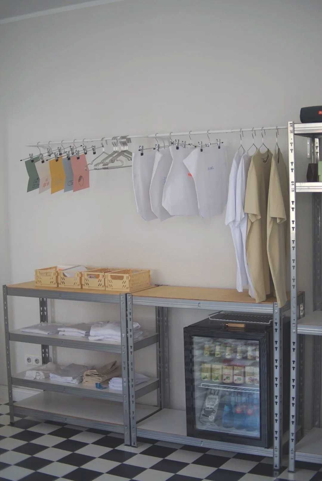 Lagerregal mit bunten Papieren, Kleidungsstücken und Boxen, Kühlschrank mit Getränken in einem Raum