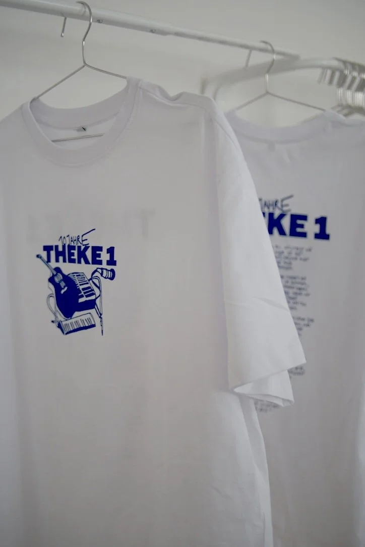 Weißes T-Shirt mit blauer Grafik und Text, für das Jubiläum der saarländischen Band "Theke 1"