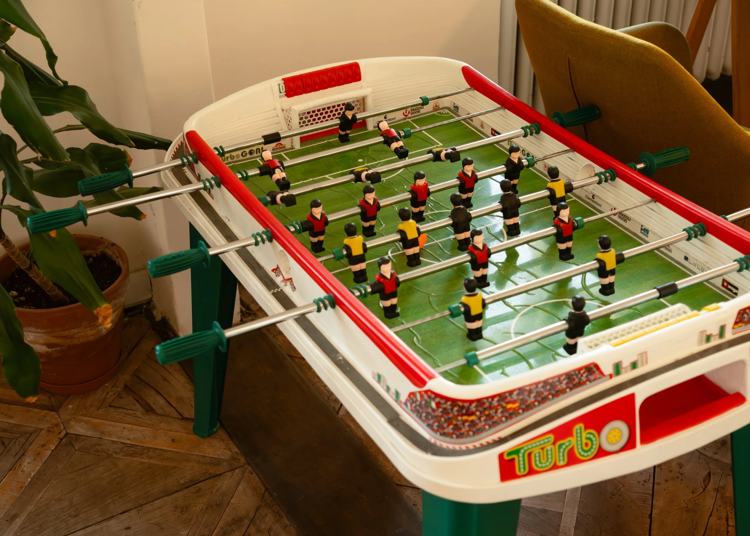 Tabletop foosball game at Controvento Hostel with black and yellow players on a green field, photographed by Skye J Blount.