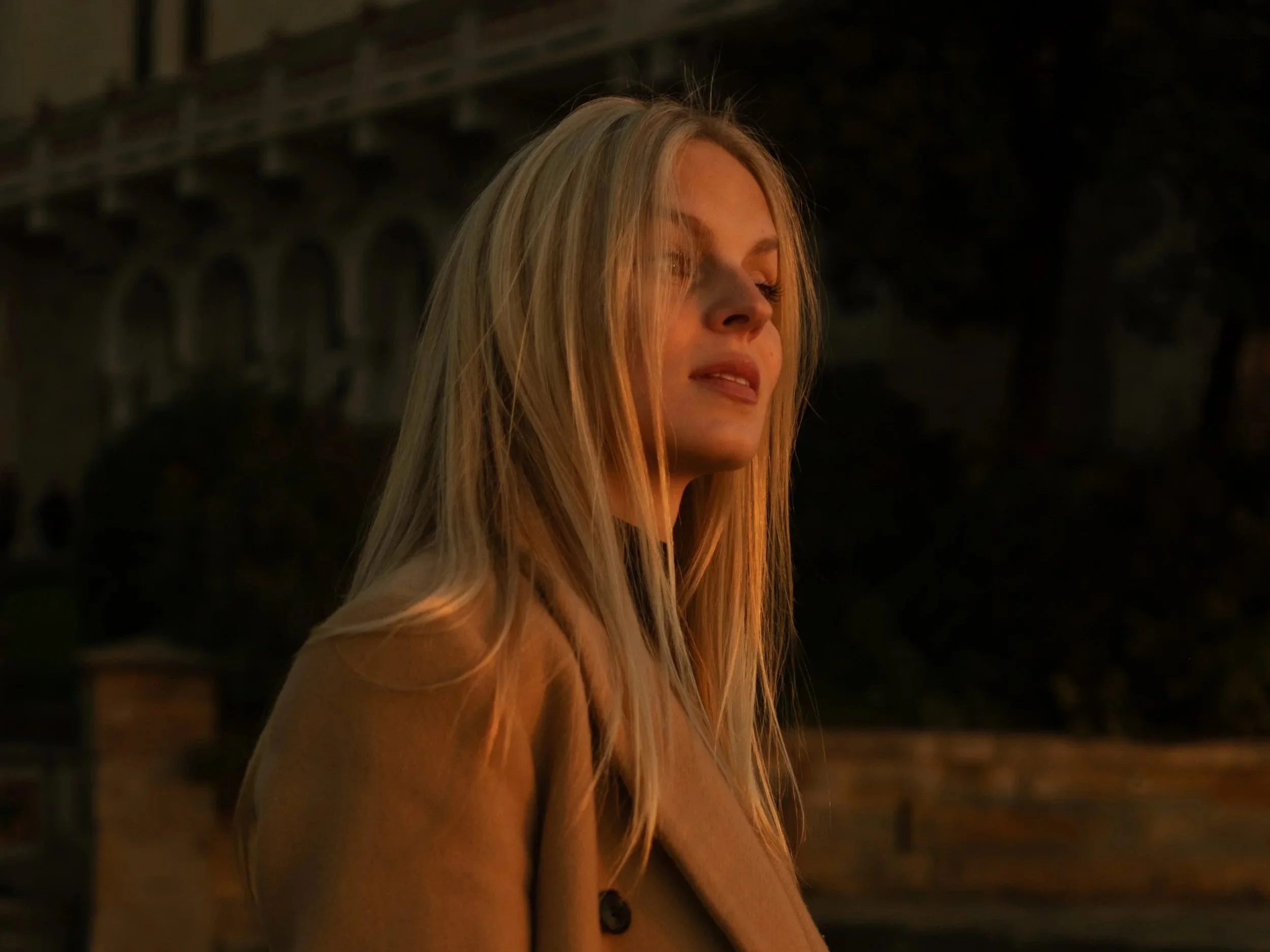 Portrait of a woman with long blonde hair standing outdoors at dusk, photographed by Skye J Blount.