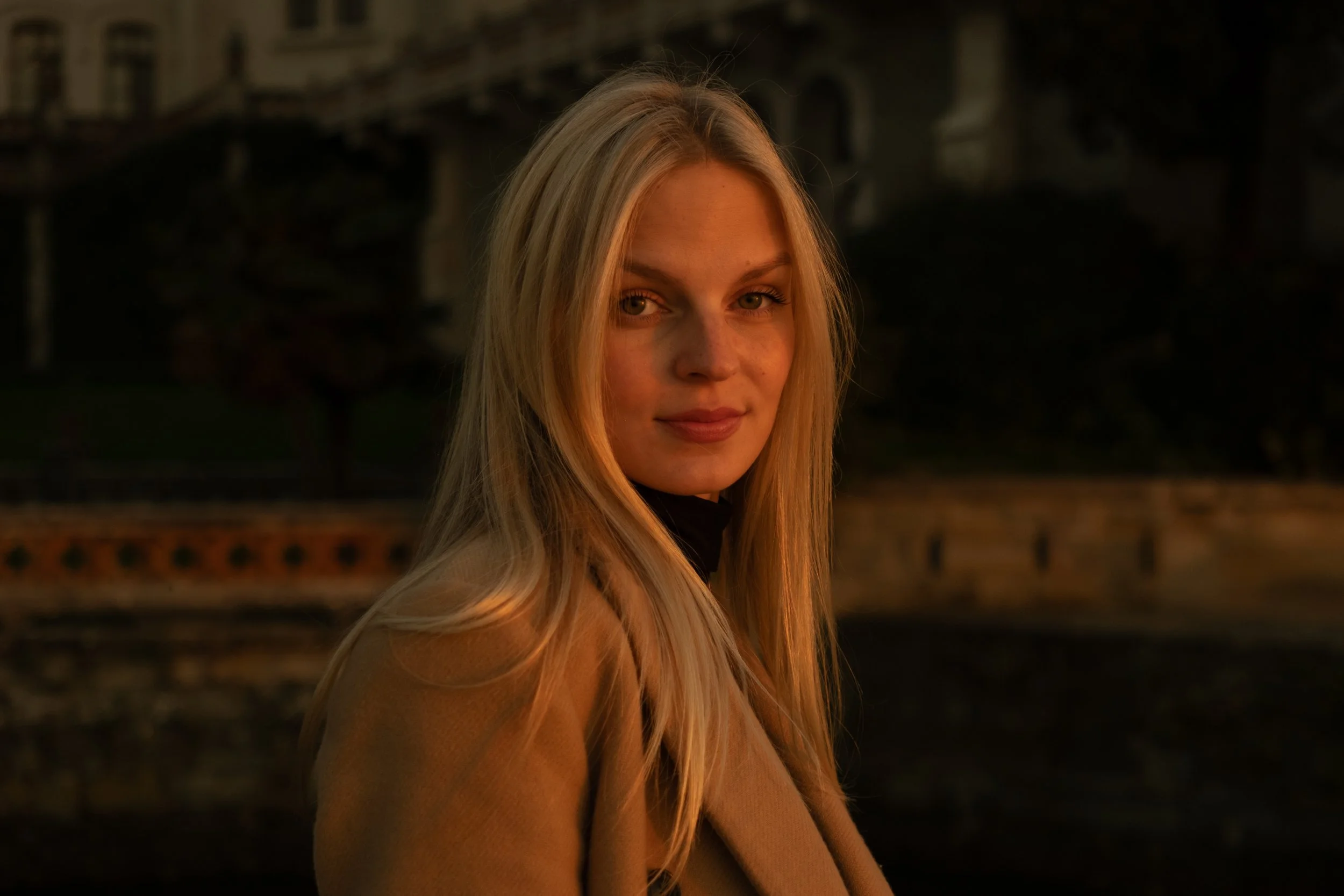 Portrait of a woman with long blonde hair wearing a tan coat, standing outdoors at sunset, photographed by Skye J Blount.
