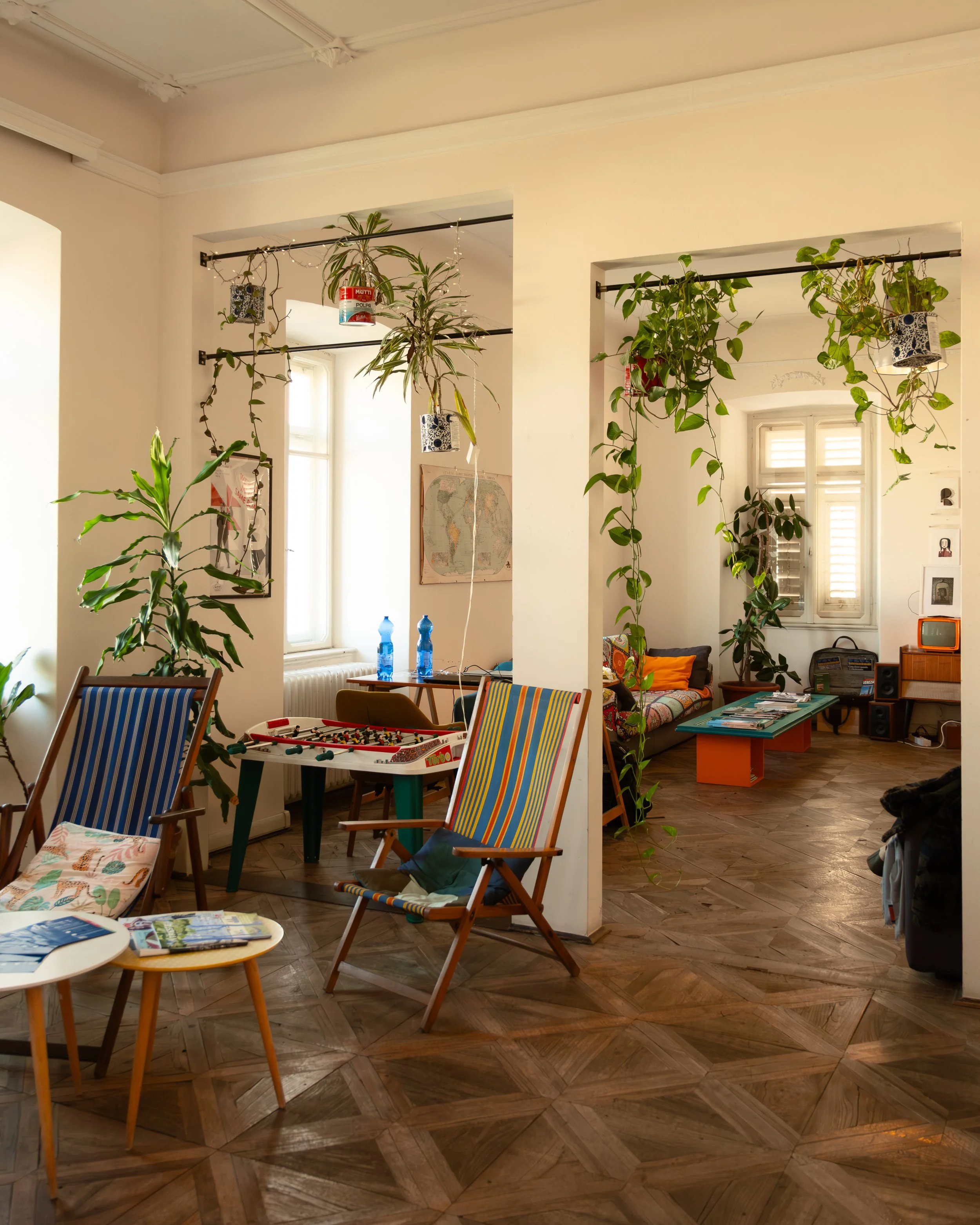 Interior photo of the living room at Controvento Hostel featuring plants, wooden chairs, a foosball table, and a sofa with coffee table, photographed by Skye J Blount.