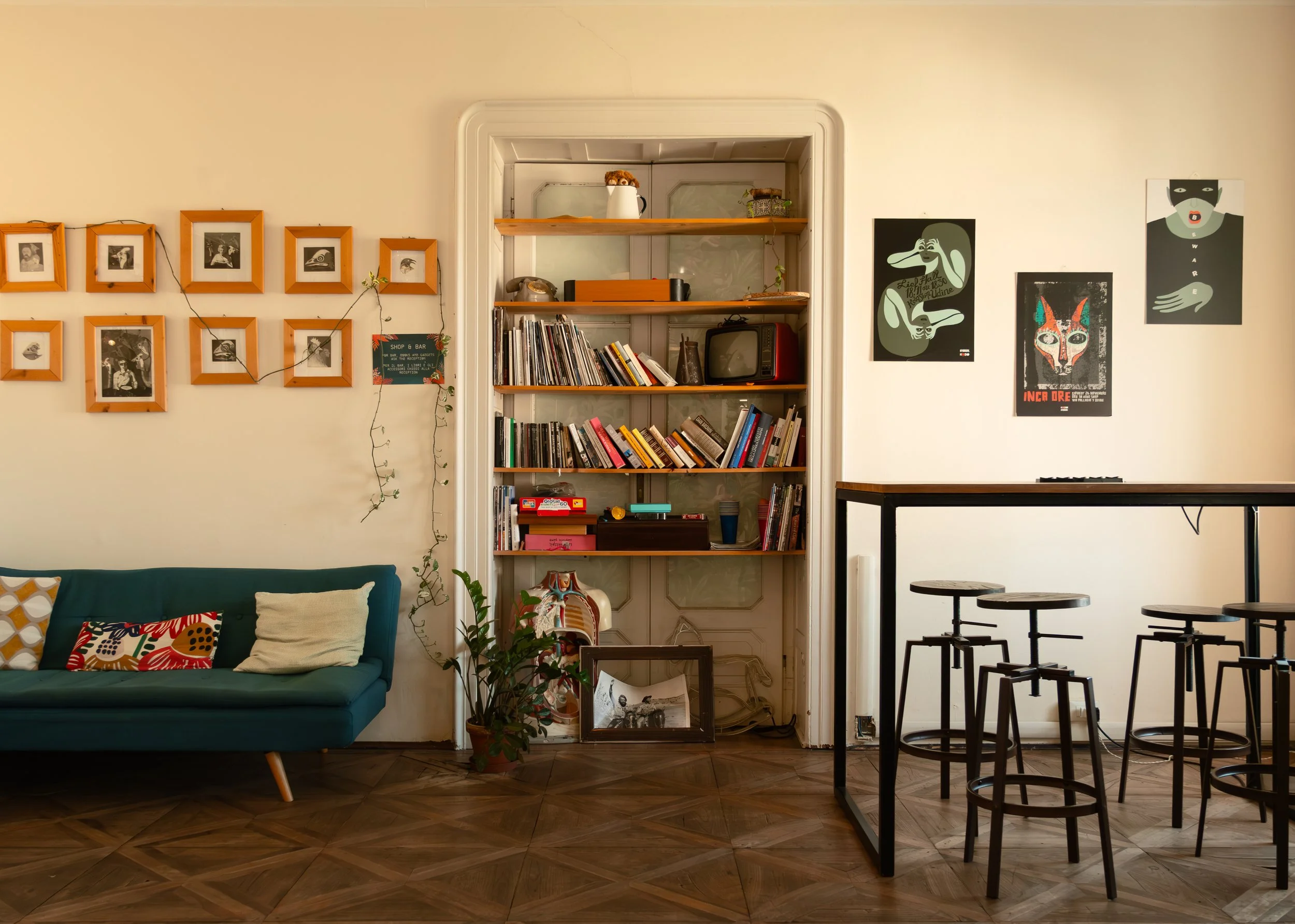 Interior of Controvento Hostel living room featuring teal sofa, decorative pillows, framed photos, bookshelf, and bar-height table with stools, photographed by Skye J Blount.