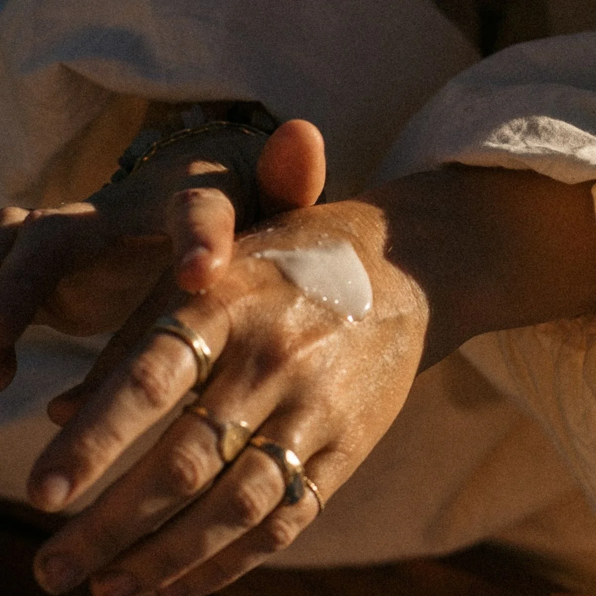 A person applying cream to their hand, adorned with multiple rings, with a darker skin tone.