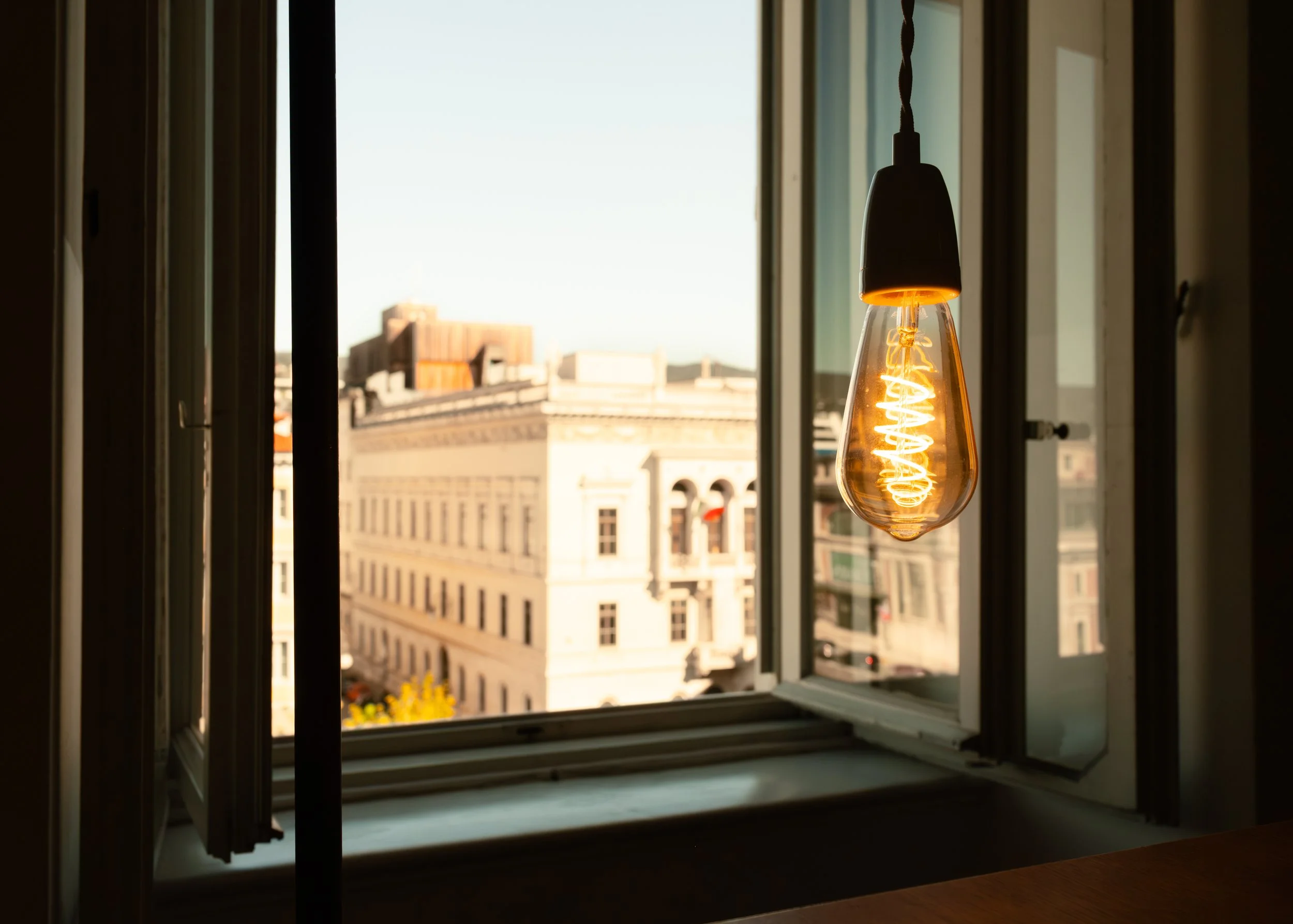 Decorative hanging lightbulb in the lounge at Controvento Hostel with cityscape visible through an open window, photographed by Skye J Blount.