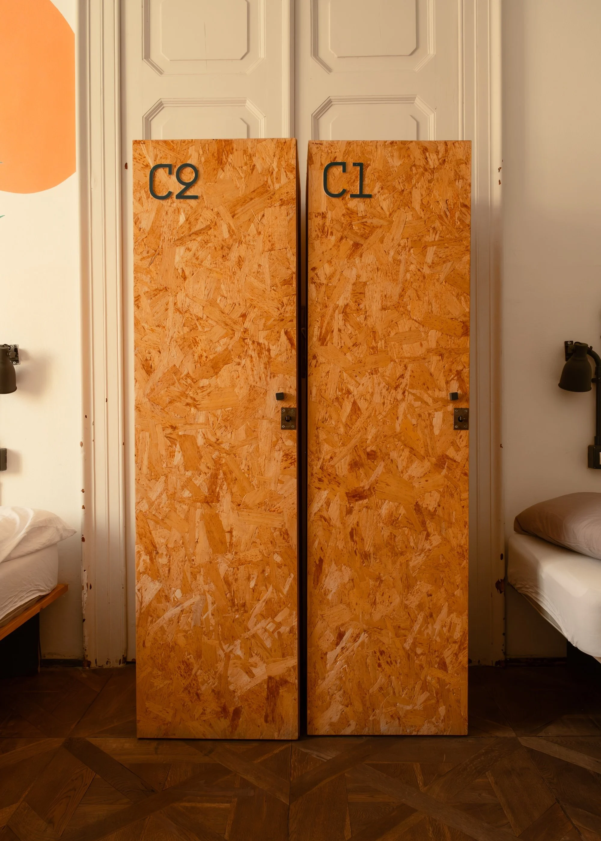 Interior photo of a room at Controvento Hostel featuring two wooden lockers labeled ‘C1’ and ‘C2’ with beds on each side, photographed by Skye J Blount.