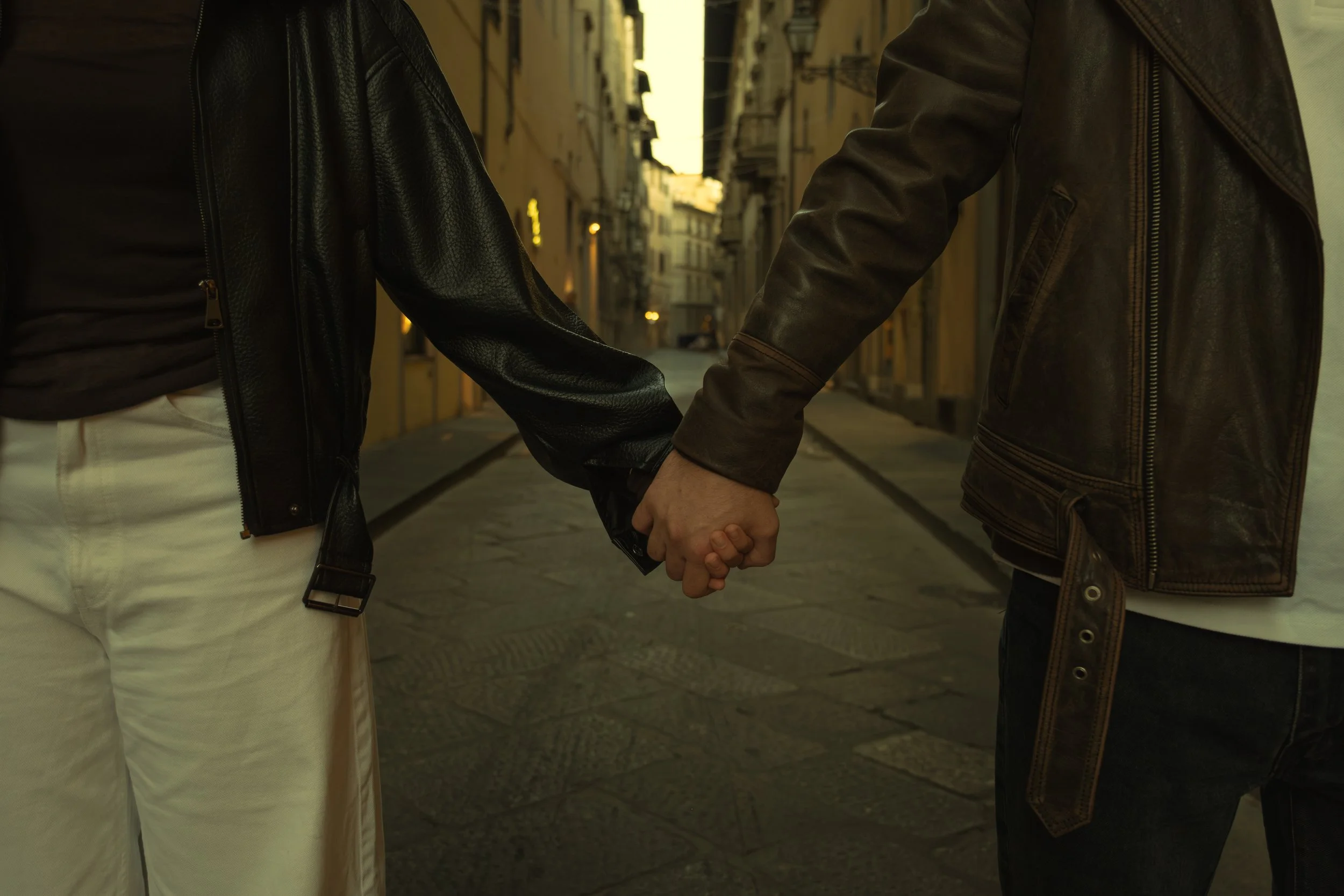 Cinematic portrait of two people holding hands in an alleyway at sunset, wearing leather jackets and pants, photographed by Skye J Blount.