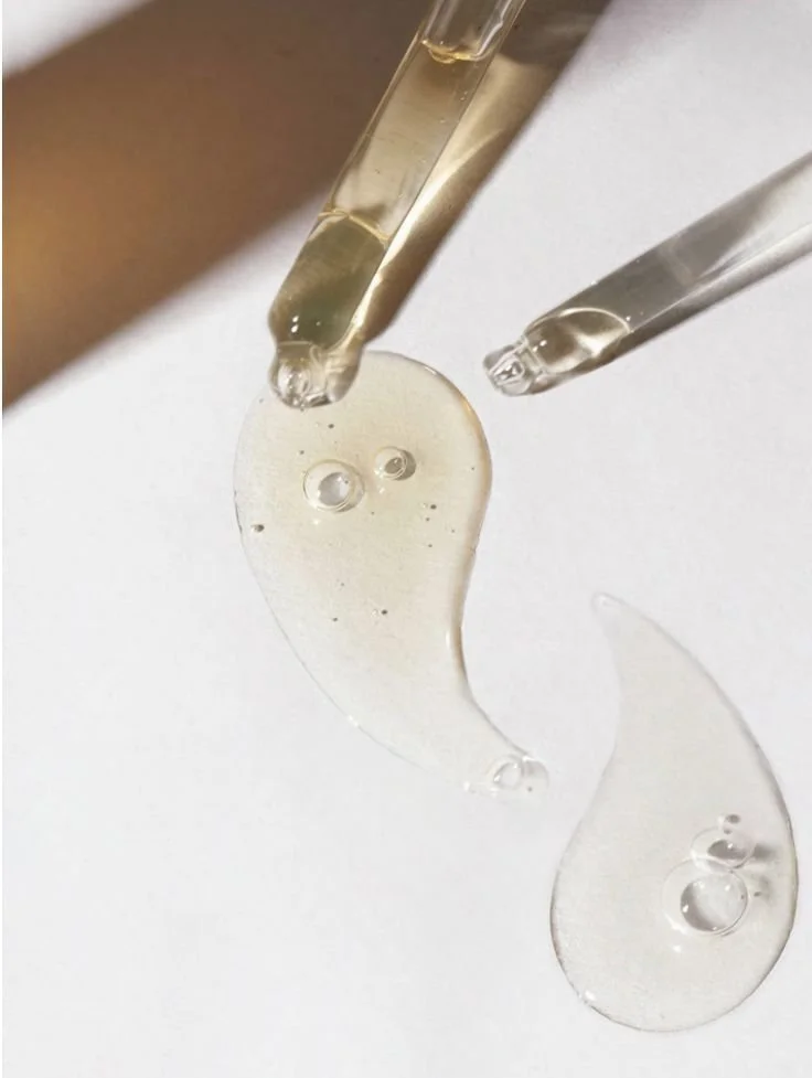 Two glass pipettes dispensing a clear serum onto a white surface.