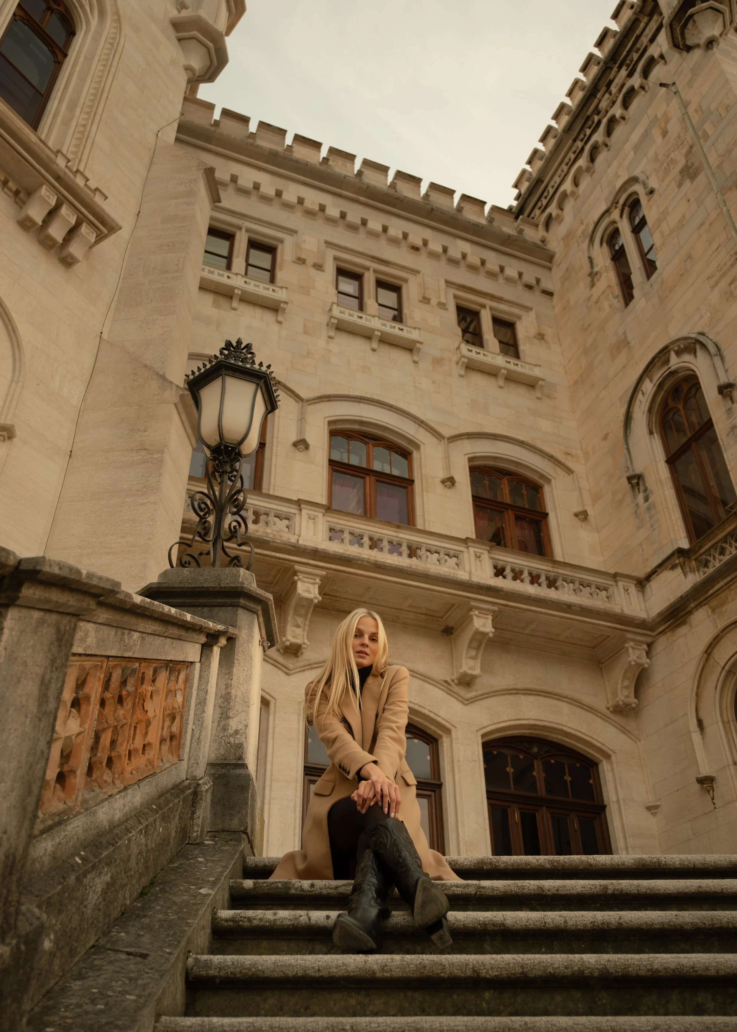Portrait of a woman with long blonde hair sitting on stone steps in front of a castle, photographed by Skye J Blount.