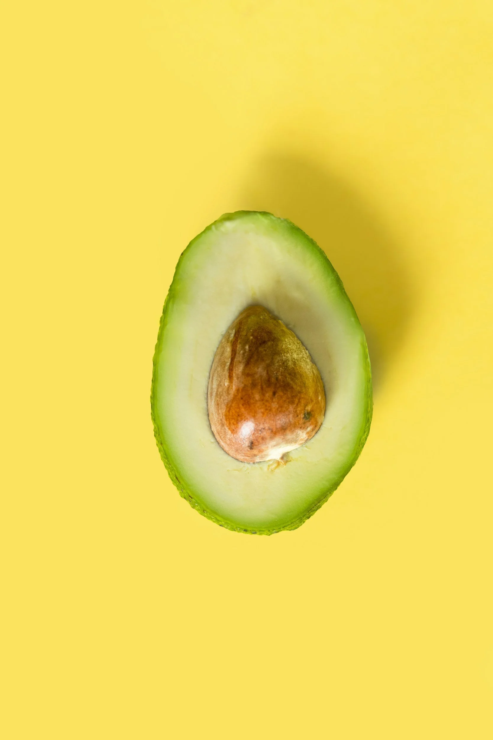 Half of a ripe avocado with seed in a yellow background.