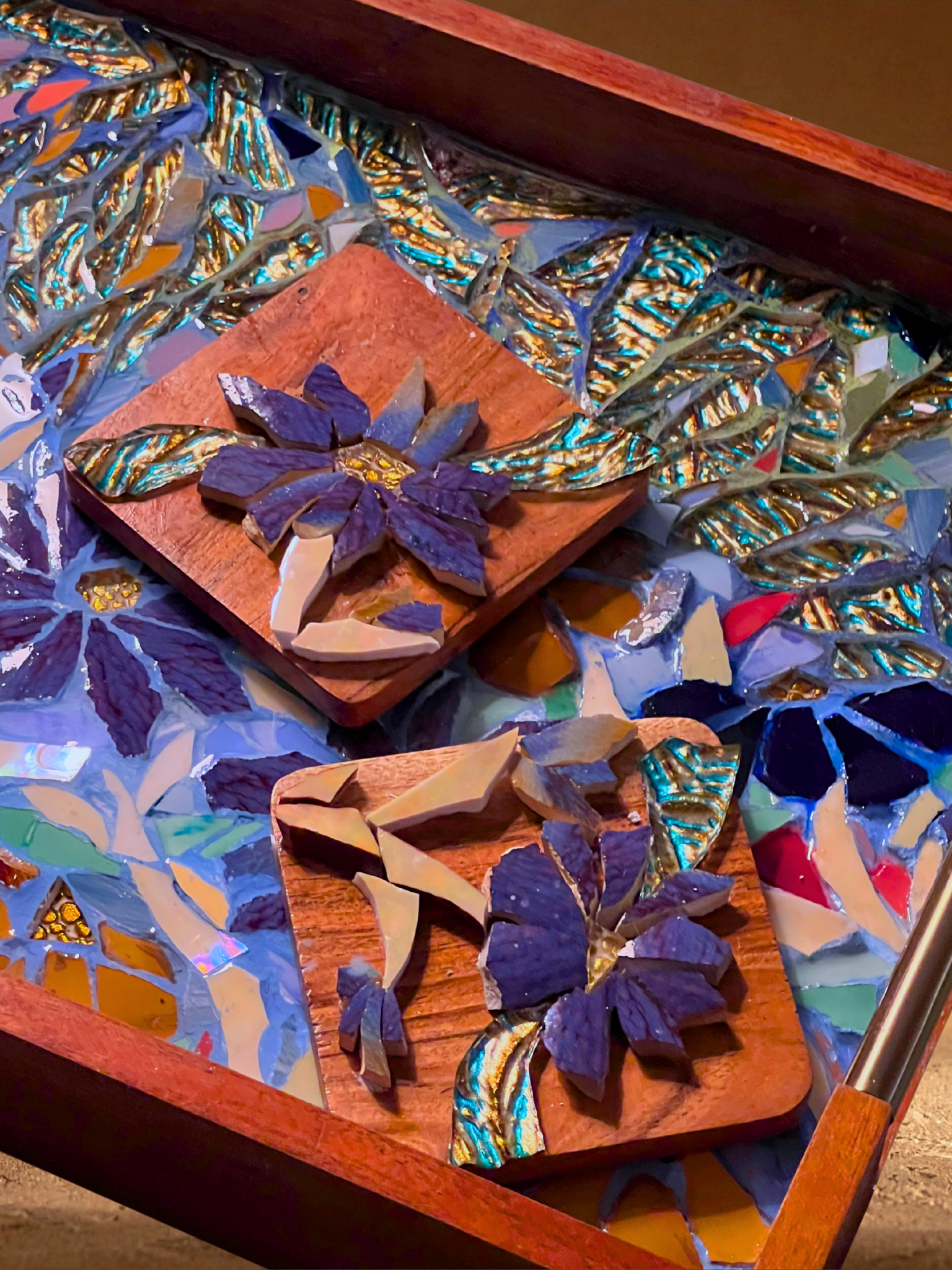 Colorful mosaic artwork featuring flowers made from broken pieces of glass and ceramic tiles, displayed on wooden boards.