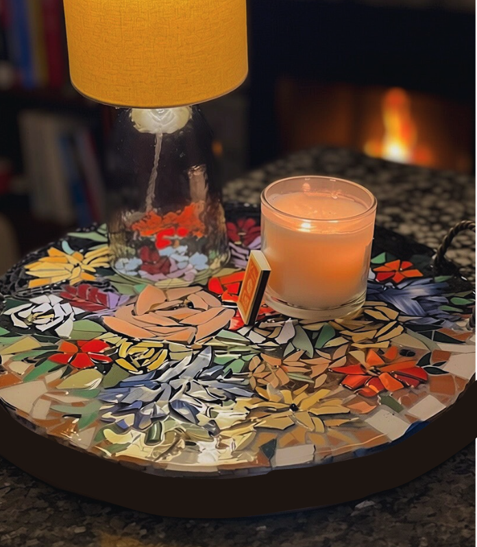 Decorative tray with a candle, a lamp, a matchbox, and a few small objects, all placed on a patterned surface with a blurred background.