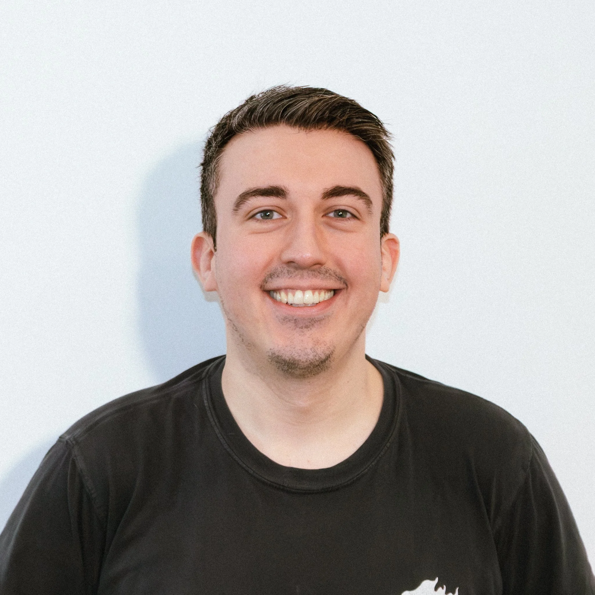 Young man smiling, wearing black sunglasses and a yellow hoodie outdoors.