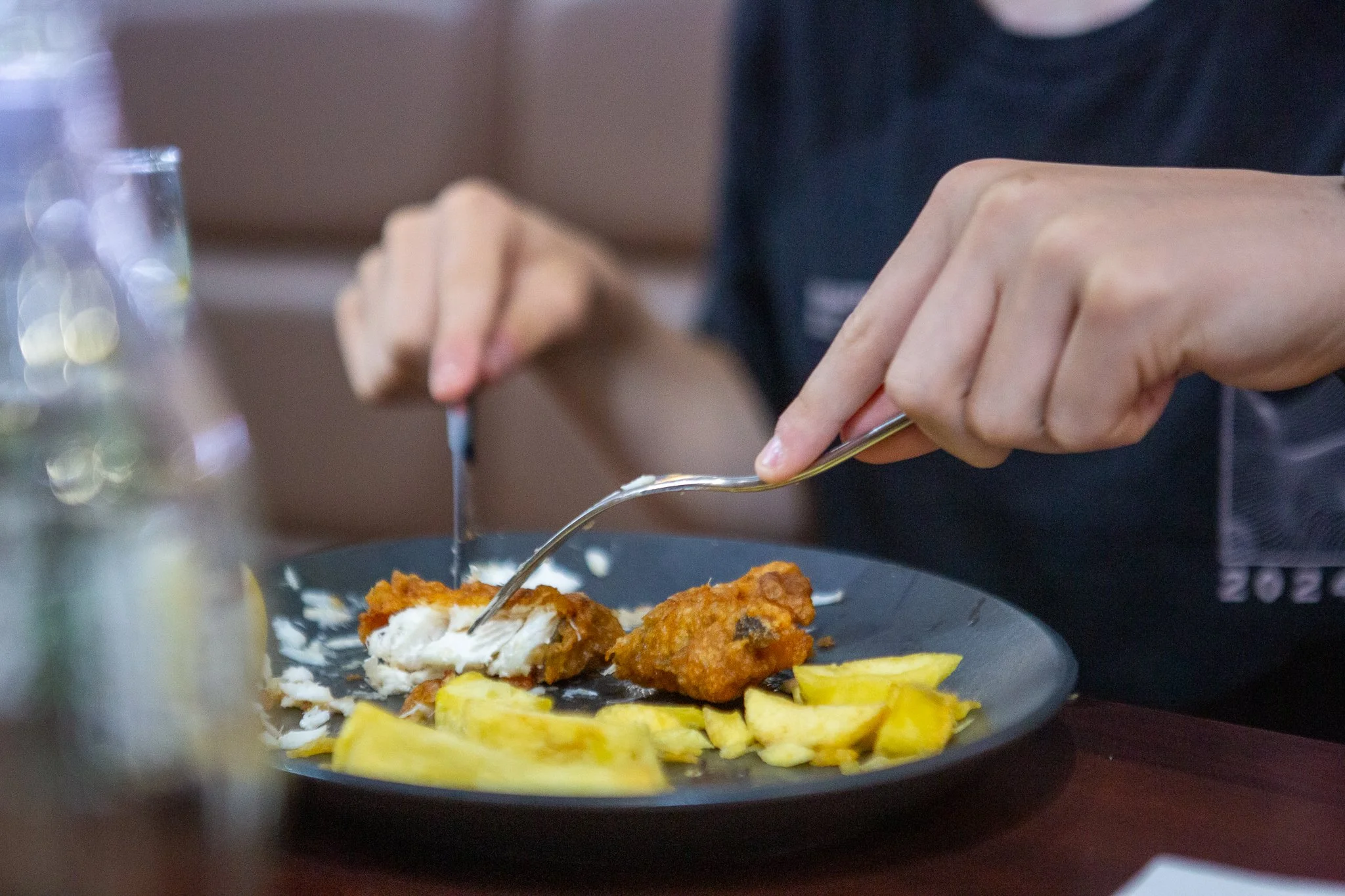 Person eating fish and chips on a black plate in a restaurant.