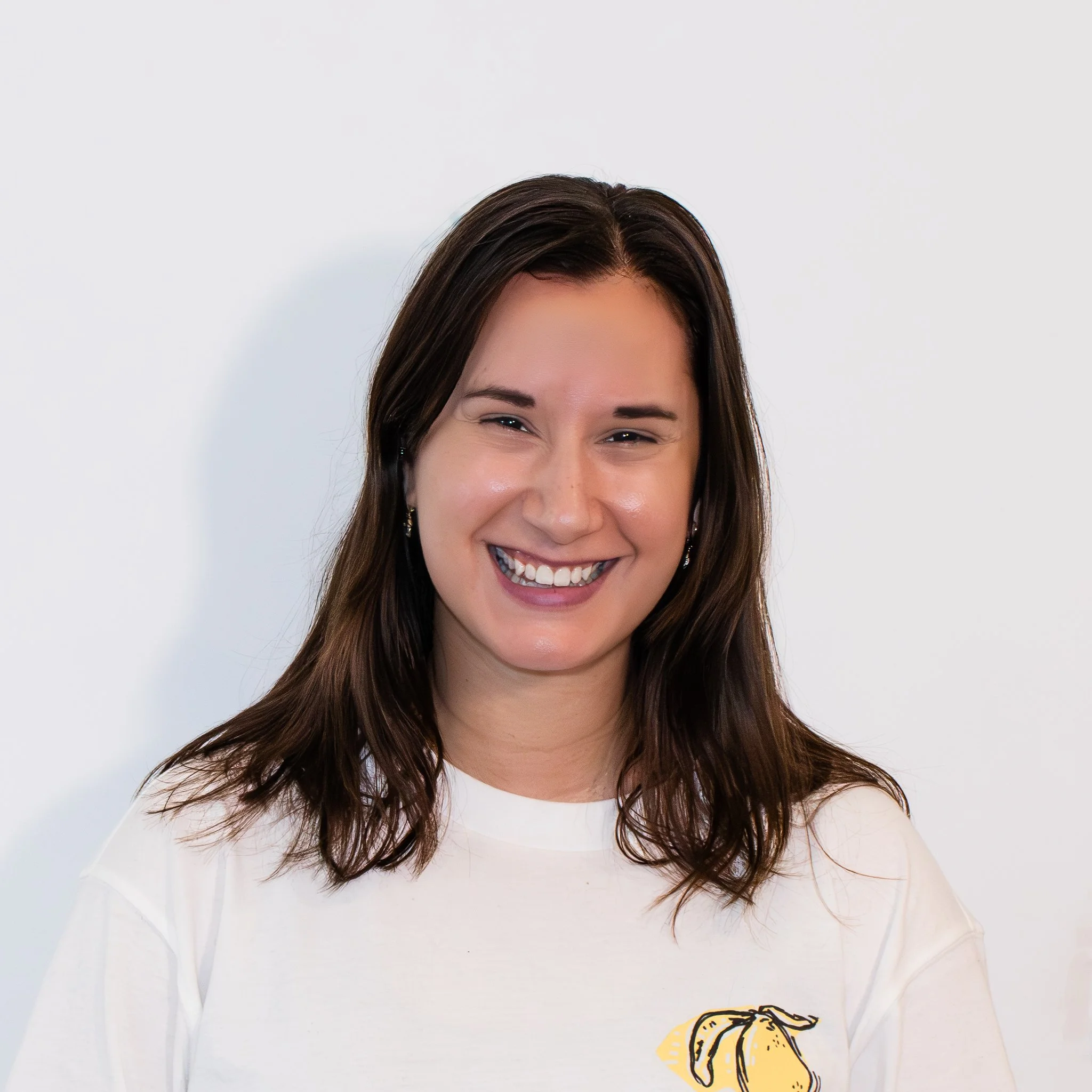 A young woman smiling outdoors in front of a decorative tiled wall with floral patterns.