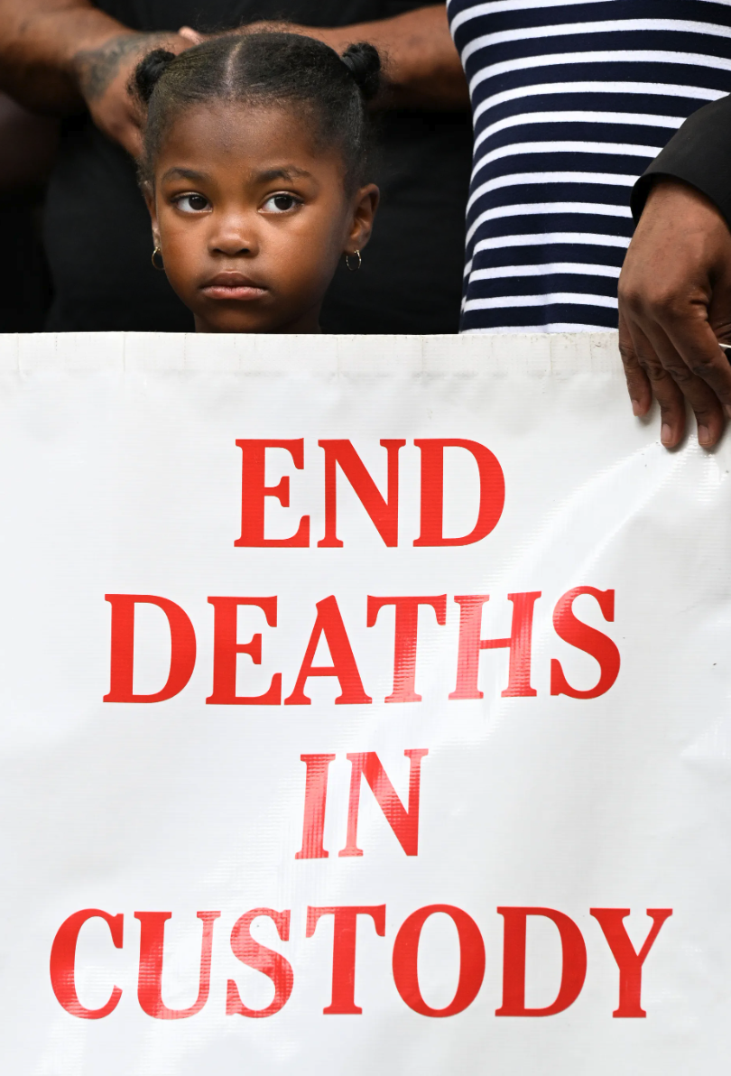 A young girl holding a sign with the message "END DEATHS IN CUSTODY" at the Notice of Intent Press Conference.