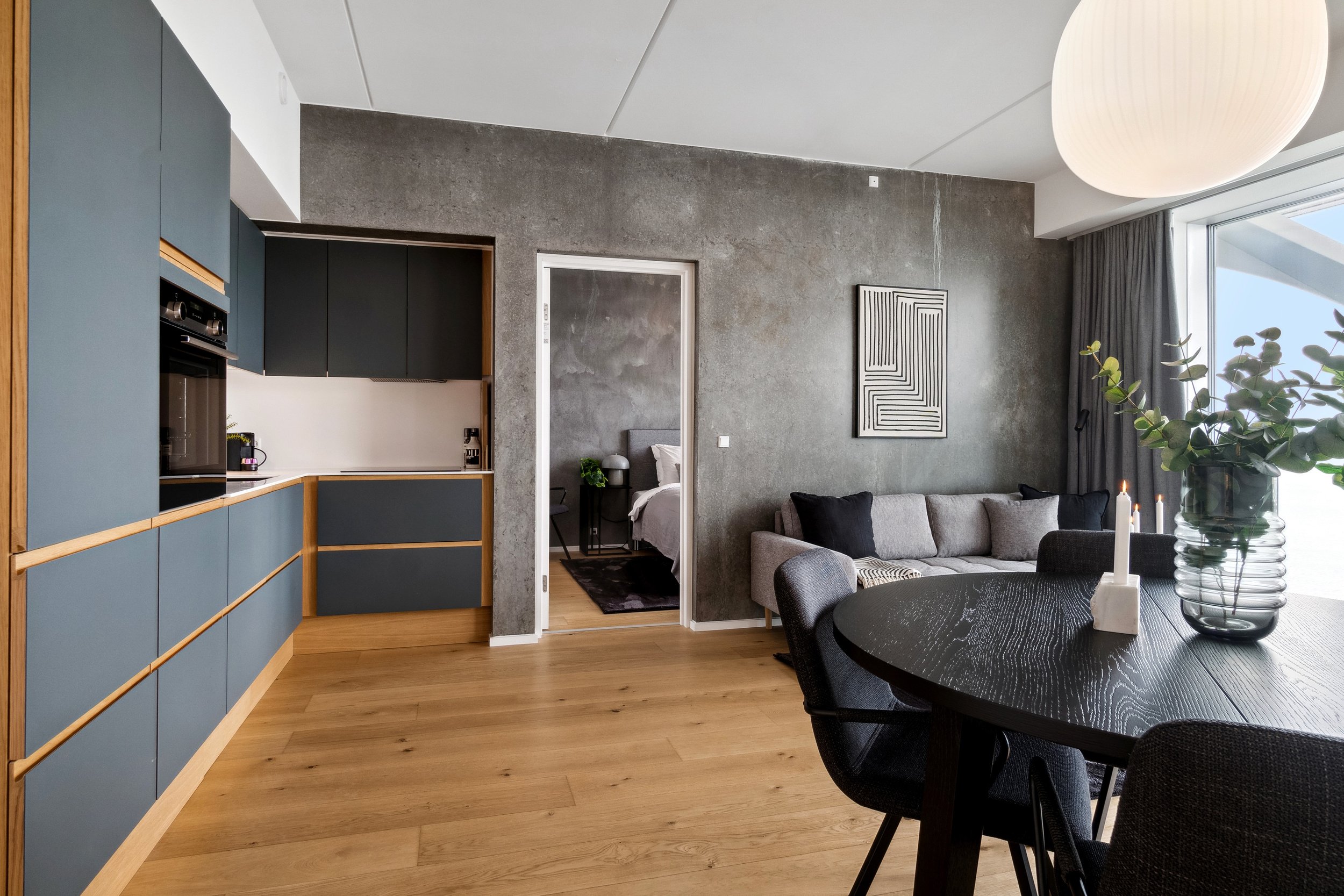 Modern living room with a gray sofa, black and gray cushions, and a black round dining table with a vase of green foliage and candles."