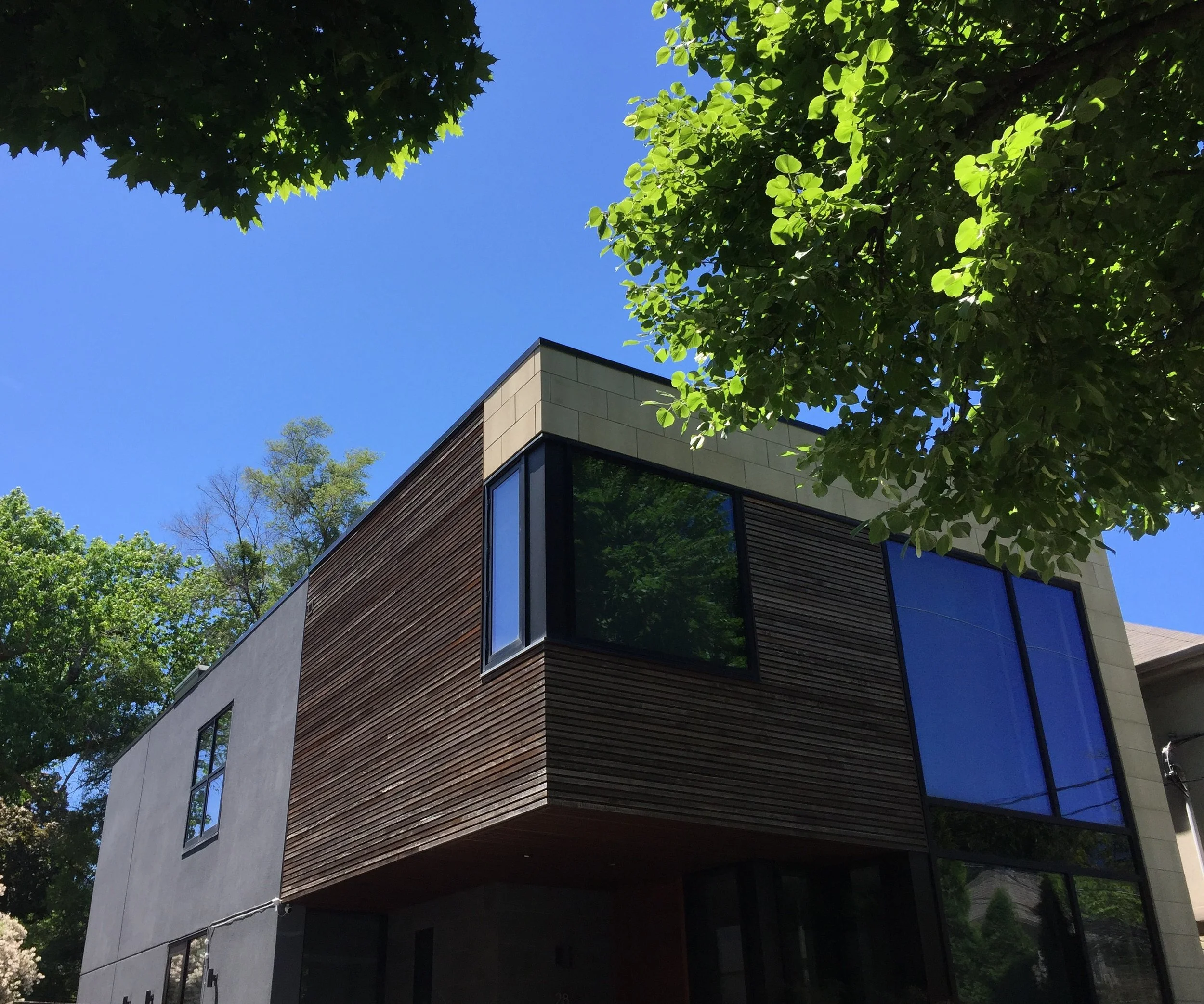 Modern house with large windows, wooden and concrete exterior, surrounded by trees and a clear blue sky in the background.