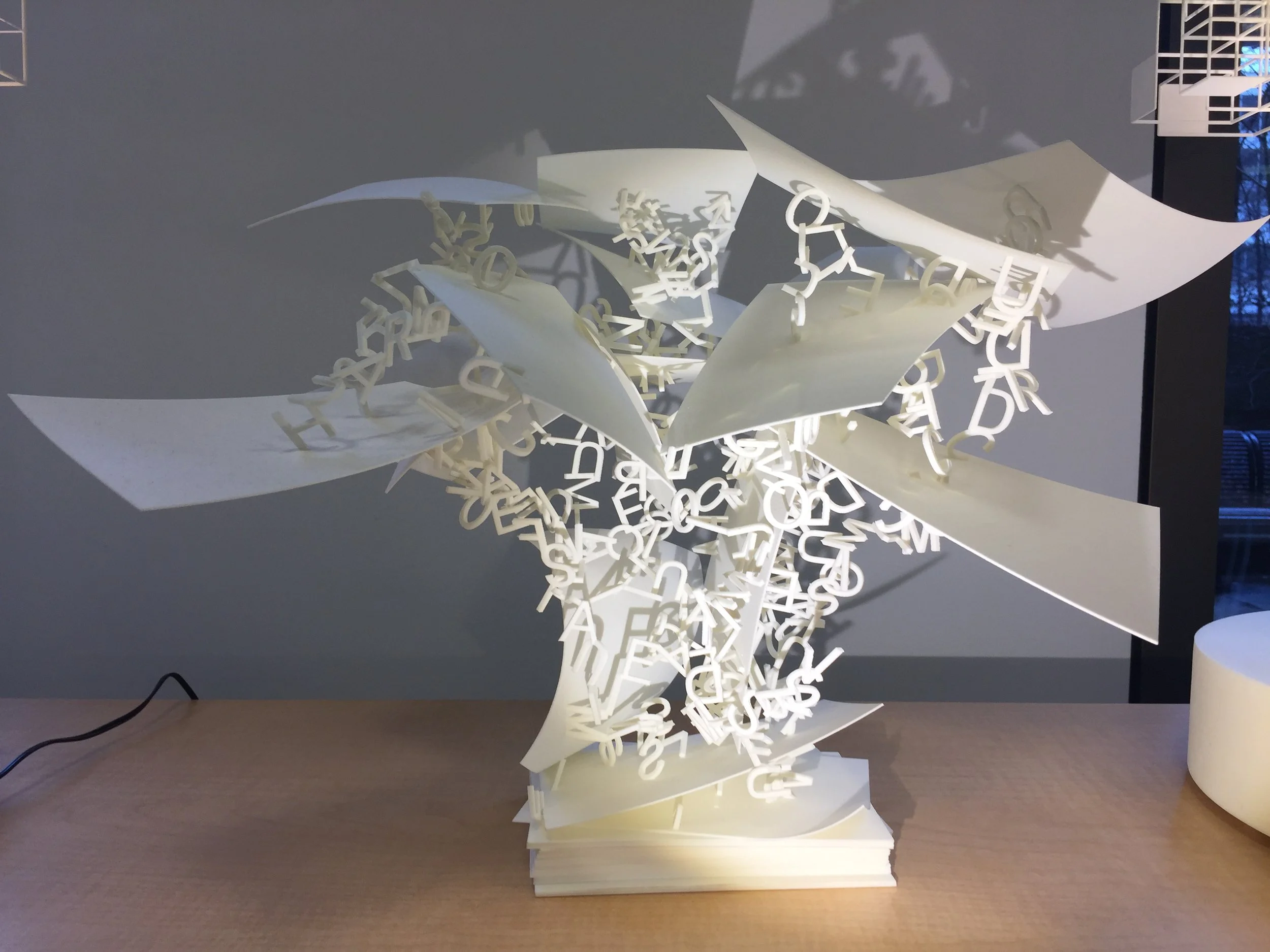 A modern white 3D generated table lamp with an artistic design featuring scattered white letters and paper-like elements protruding outward.