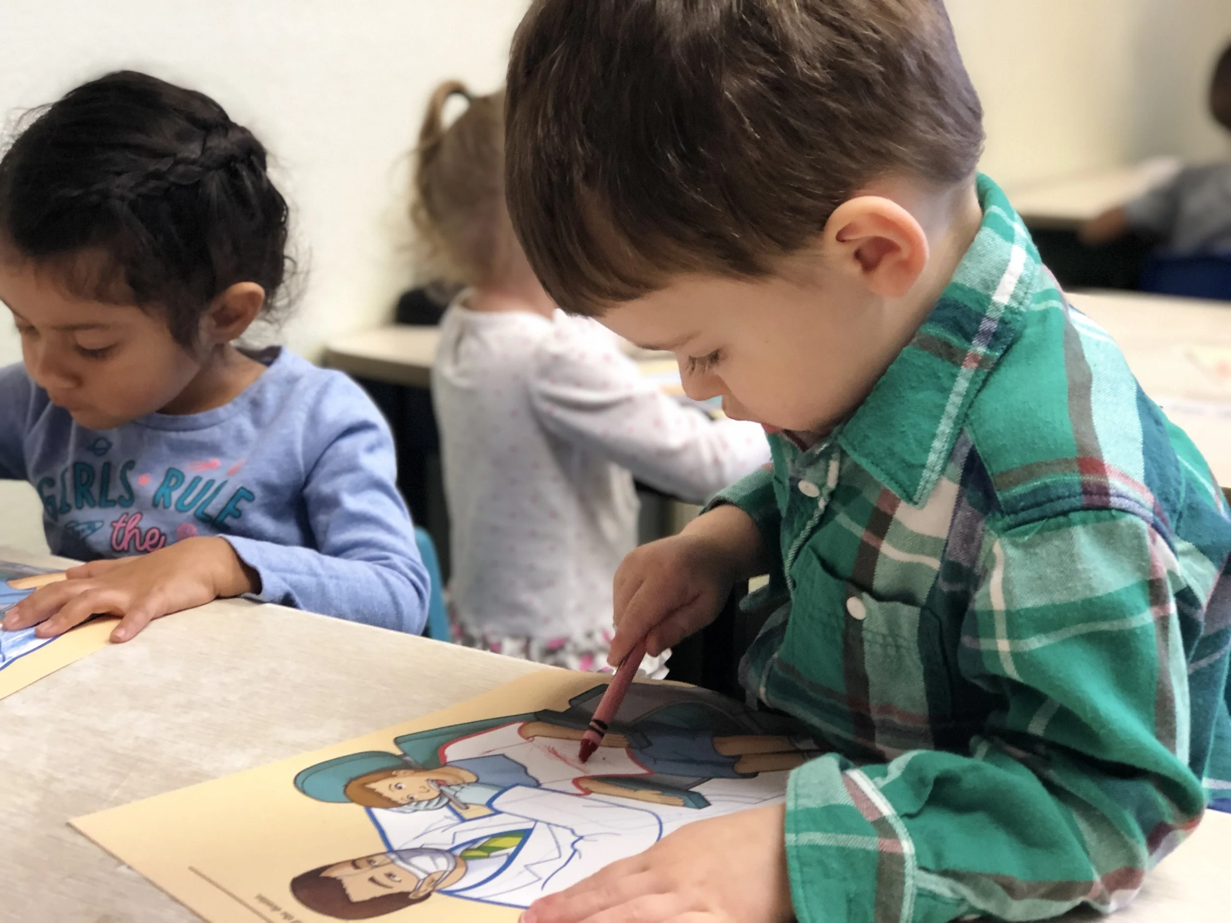 Young children sitting at tables coloring pictures of women.