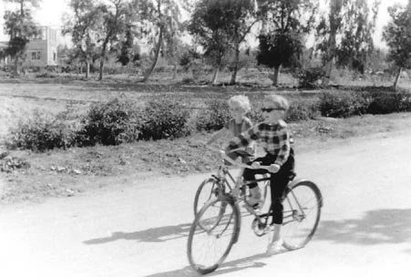 Richter children cycling on Road 20 with Taher Bey Lozi's "funhouse" seen at end of Road 82 where it intersects Road 21