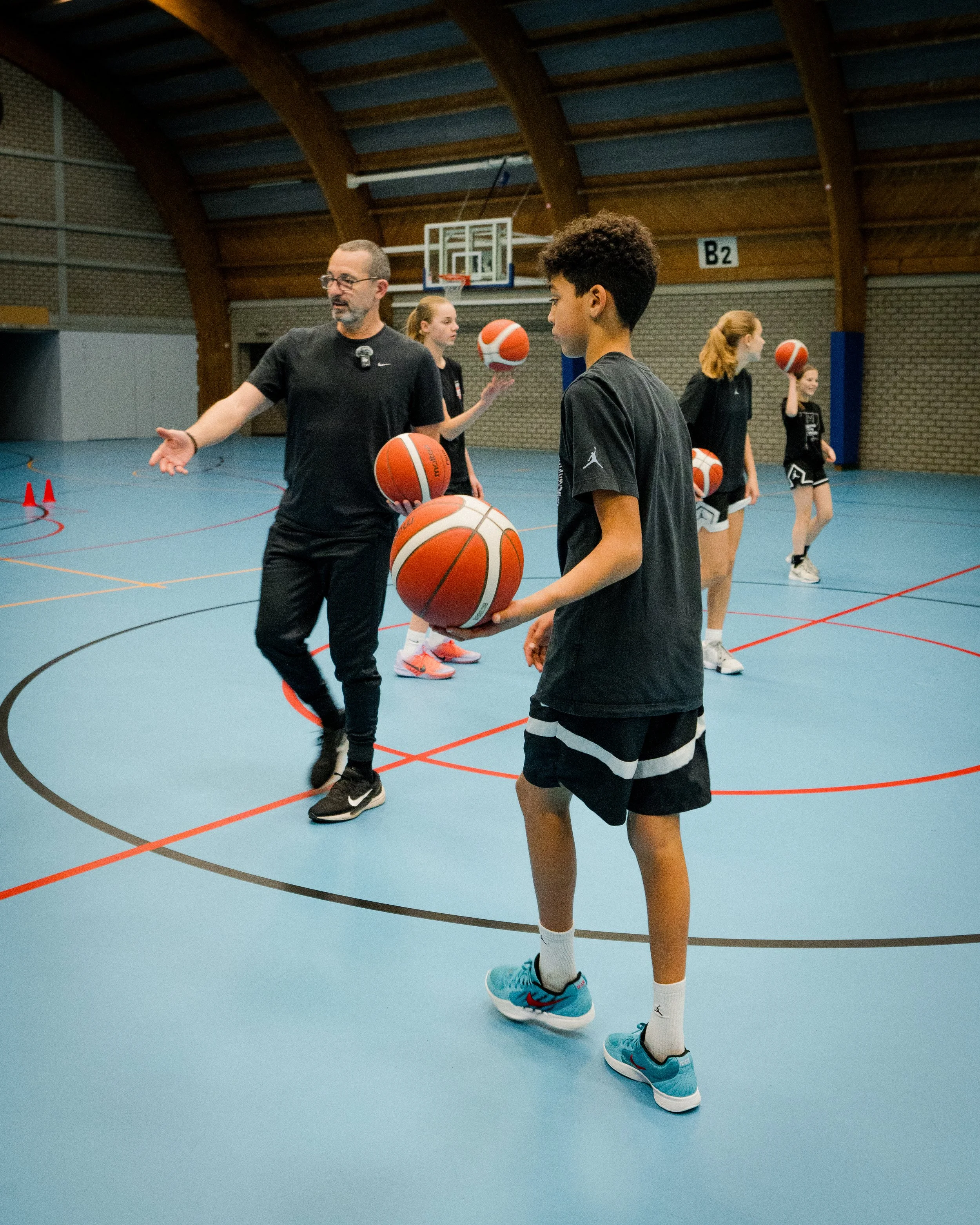 Basketball coach instructs young players during a training session inside a gymnasium.