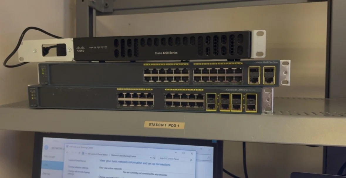 Closet shelf with three network switches and a Cisco 4200 series network device, with a computer monitor showing network information below by Wilson Michael Katsande