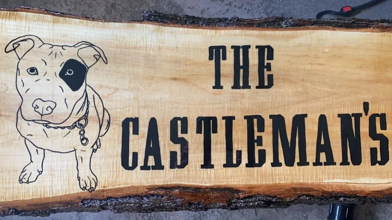 Wooden sign with a drawing of a dog wearing a collar on the left and the words 'The Castleman's' on the right.
