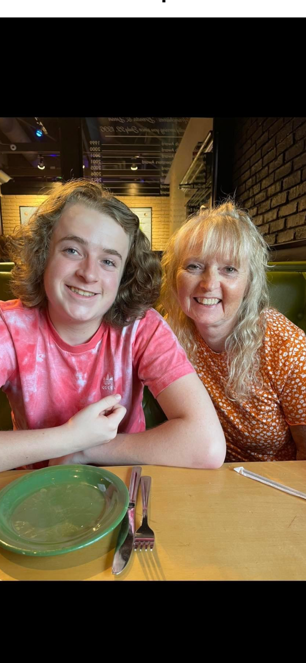 Lucas with his curly hair and his mom, Karen with long blonde hair smiling, sitting at a restaurant table with green plates and silverware.