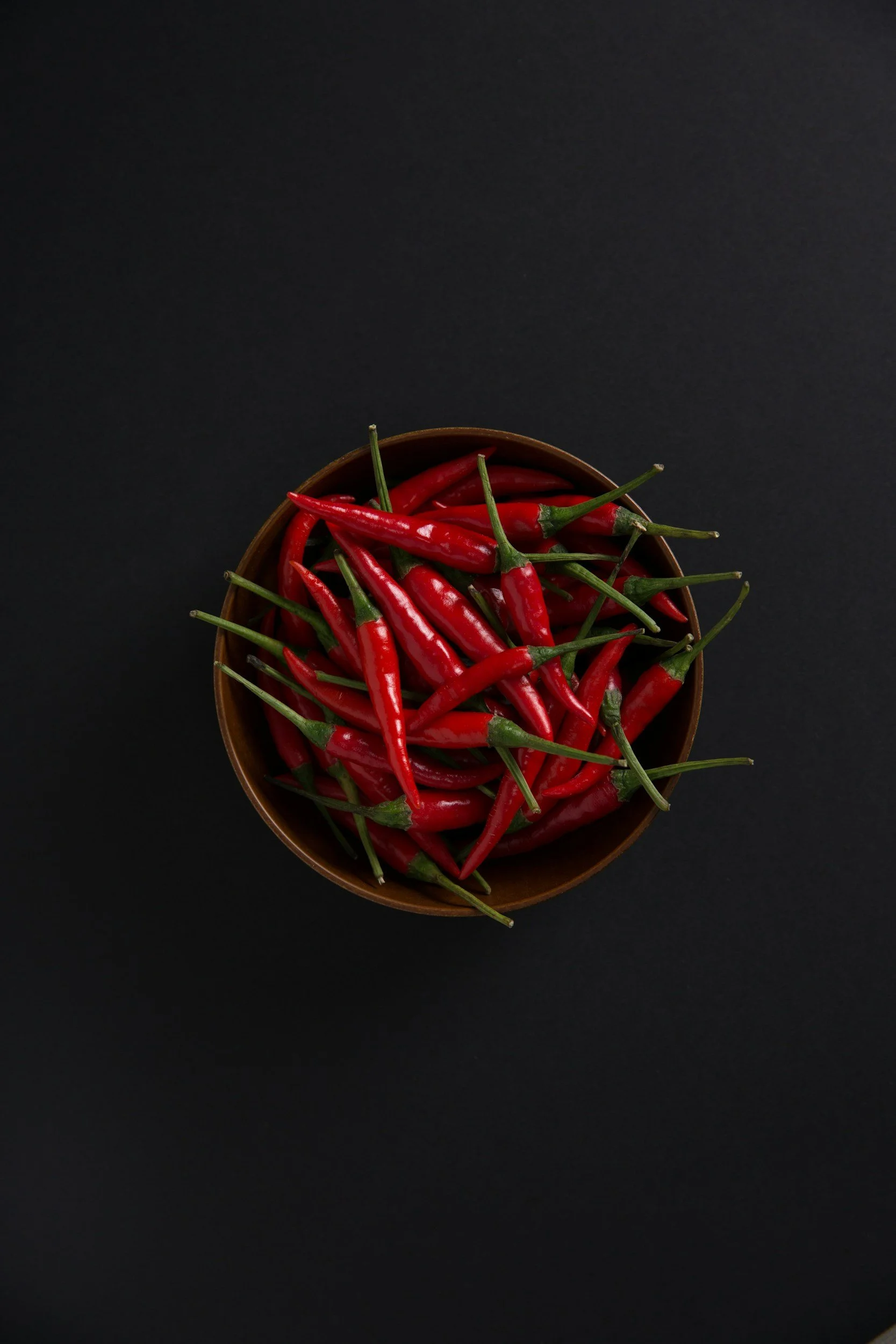 Red chili peppers in a wooden bowl on a black background