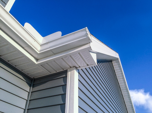 Close-up of house's white gutter and siding against a clear blue sky.