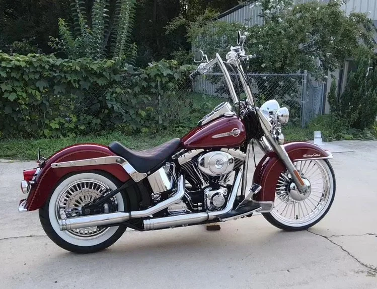 Red Harley-Davidson motorcycle parked on a driveway with a garden and a fence in the background.