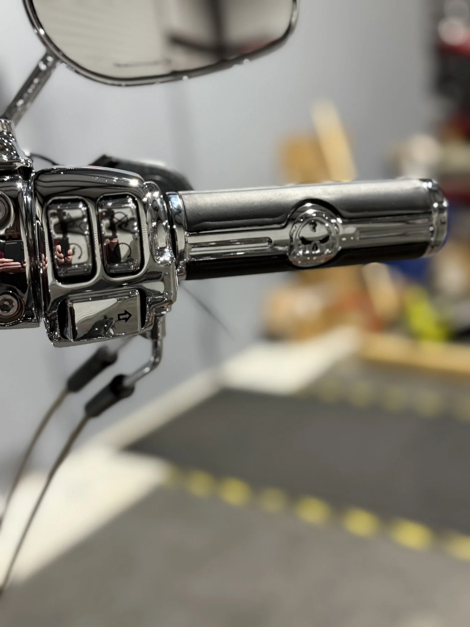 Close-up of a chrome motorcycle handlebar with a rearview mirror and control buttons, blurred background.